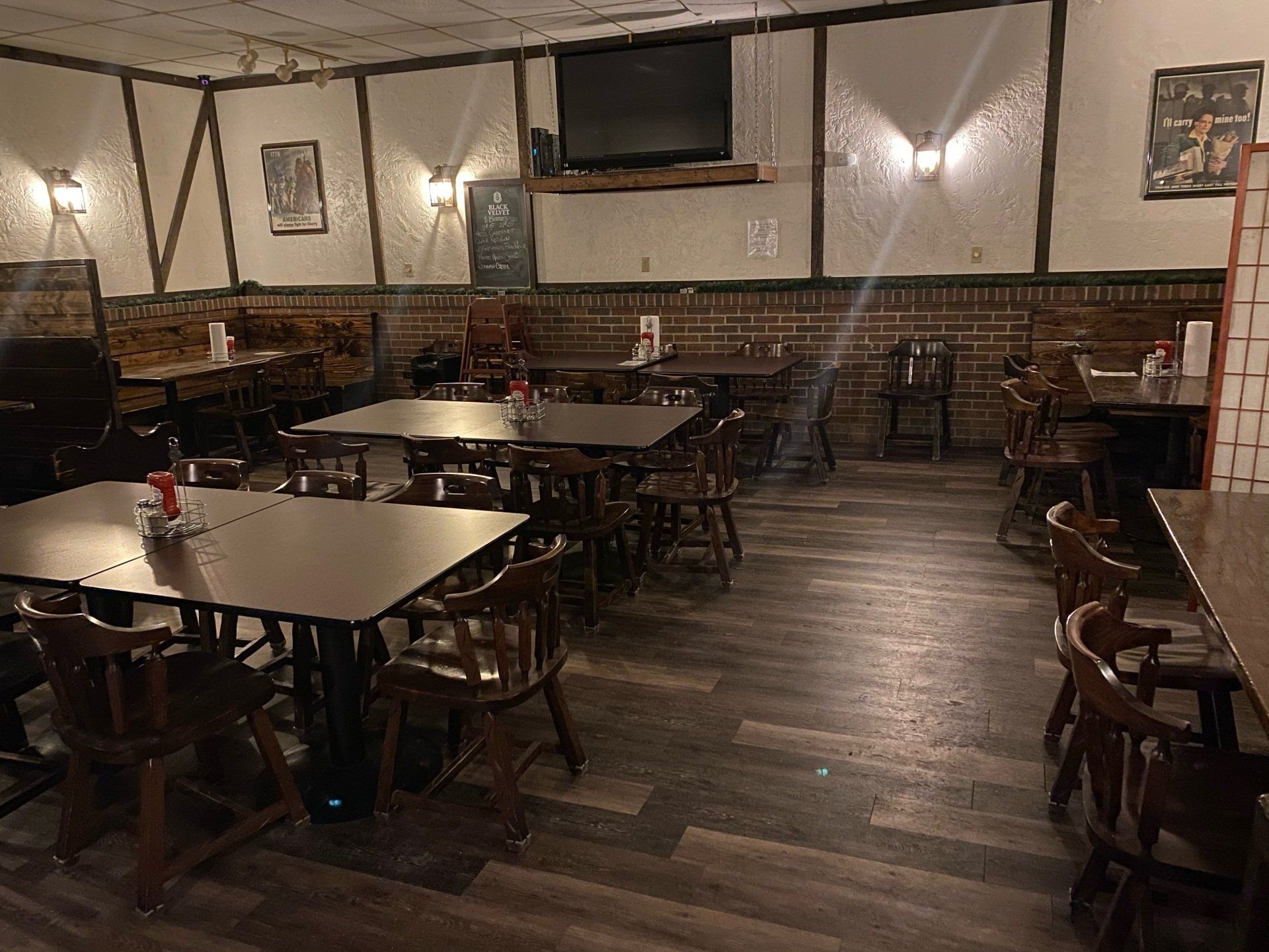 Restaurant interior with tables, chairs, and brick accents. TV and framed art on the walls.