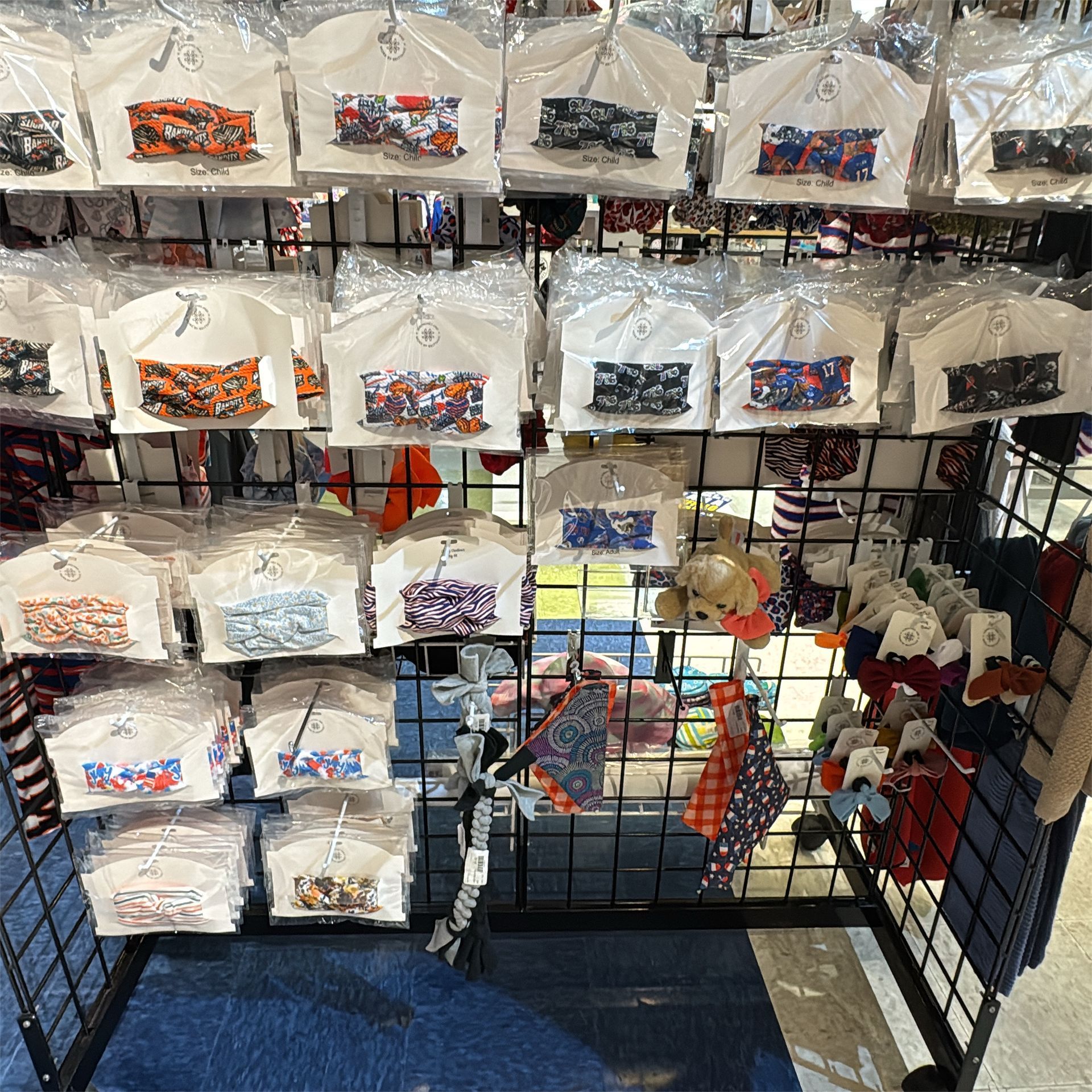 Display of packaged t-shirts with colorful designs and various hats, displayed on a black wire rack in a store.