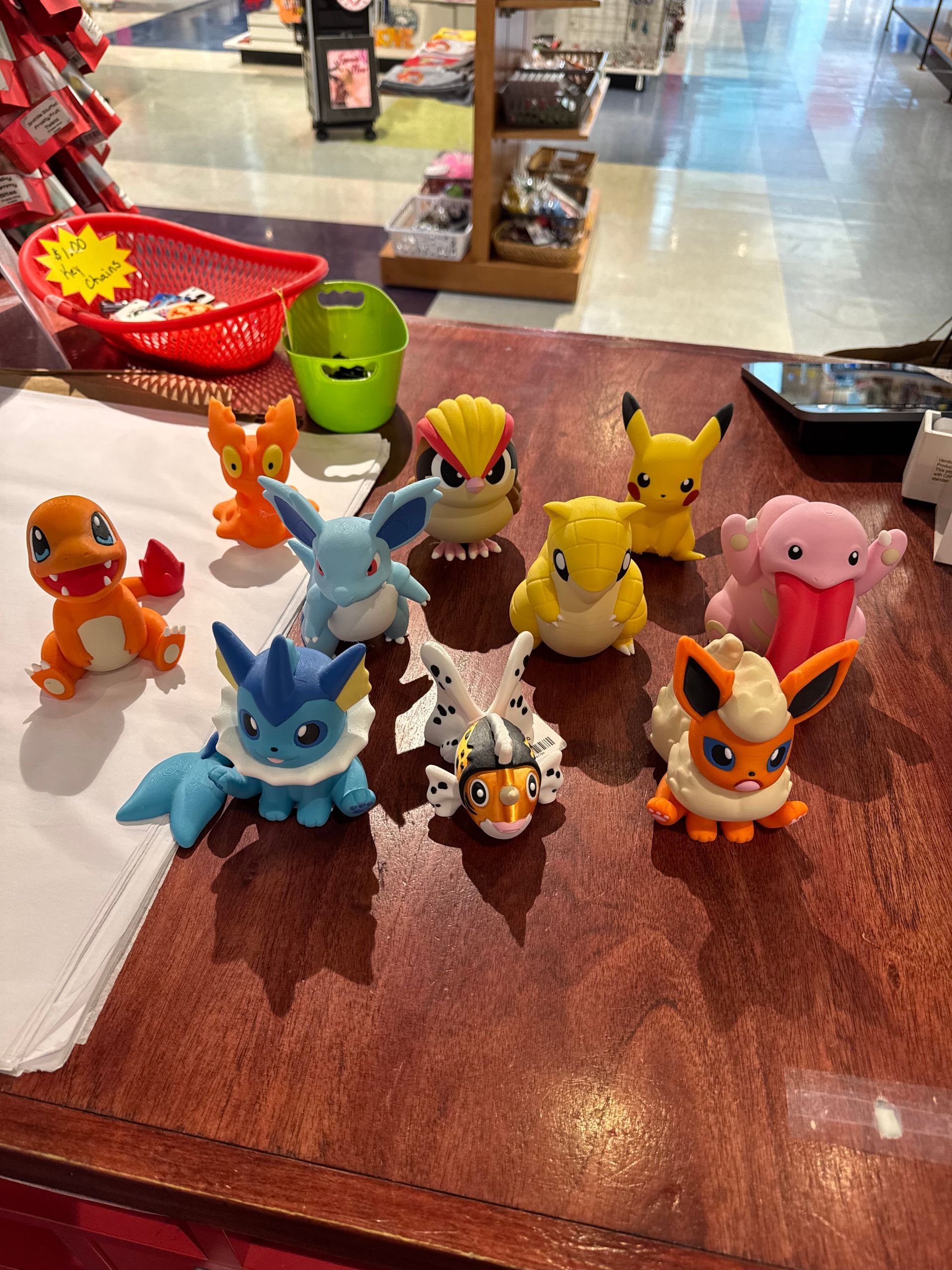Various Pokémon figurines on a countertop in a store, including Charmander, Pikachu, and Eevee evolutions.