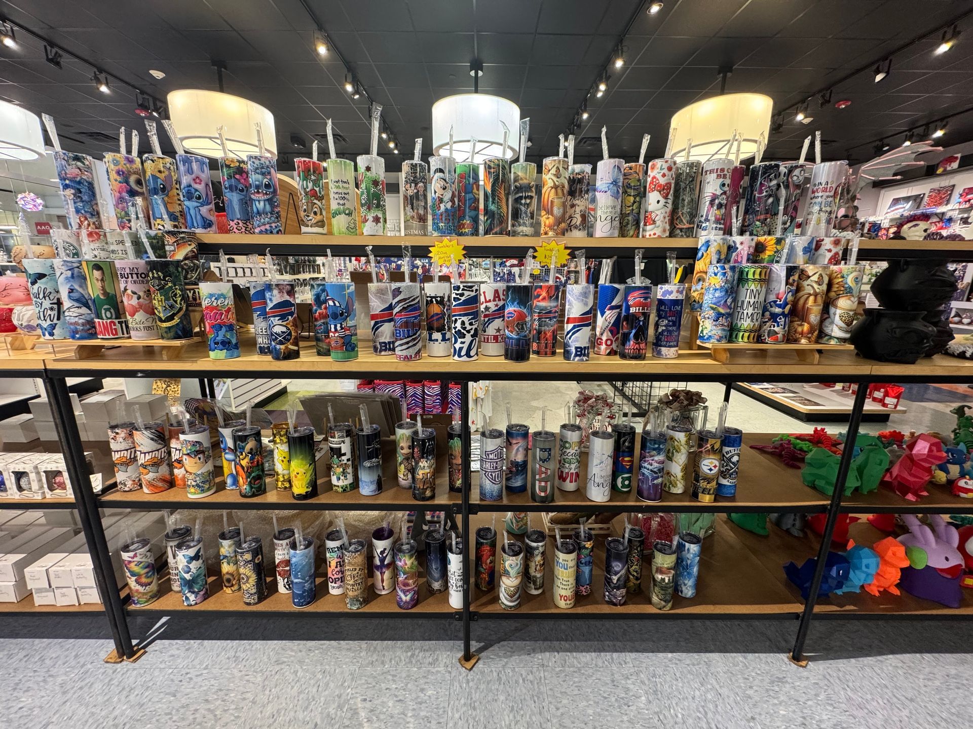 Shelves filled with various colorful, patterned cylindrical tumblers in a retail store.