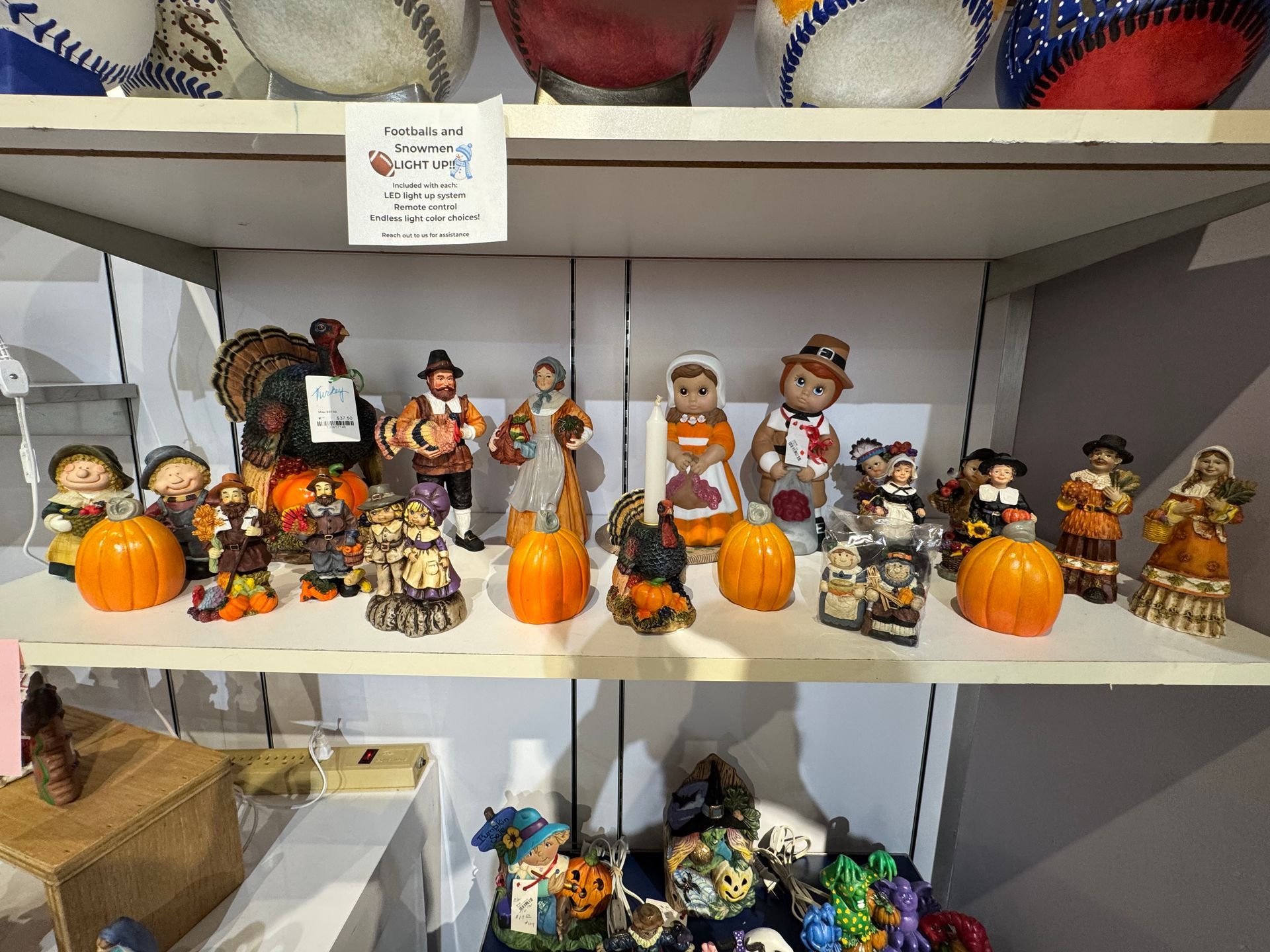 Shelves filled with Thanksgiving figurines, pumpkins, and a turkey; some are wearing pilgrim outfits.