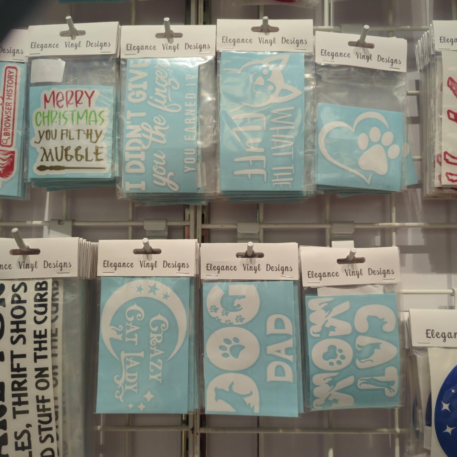 Display of vinyl decals with text and images, including holiday, cat, and paw print designs in a store.