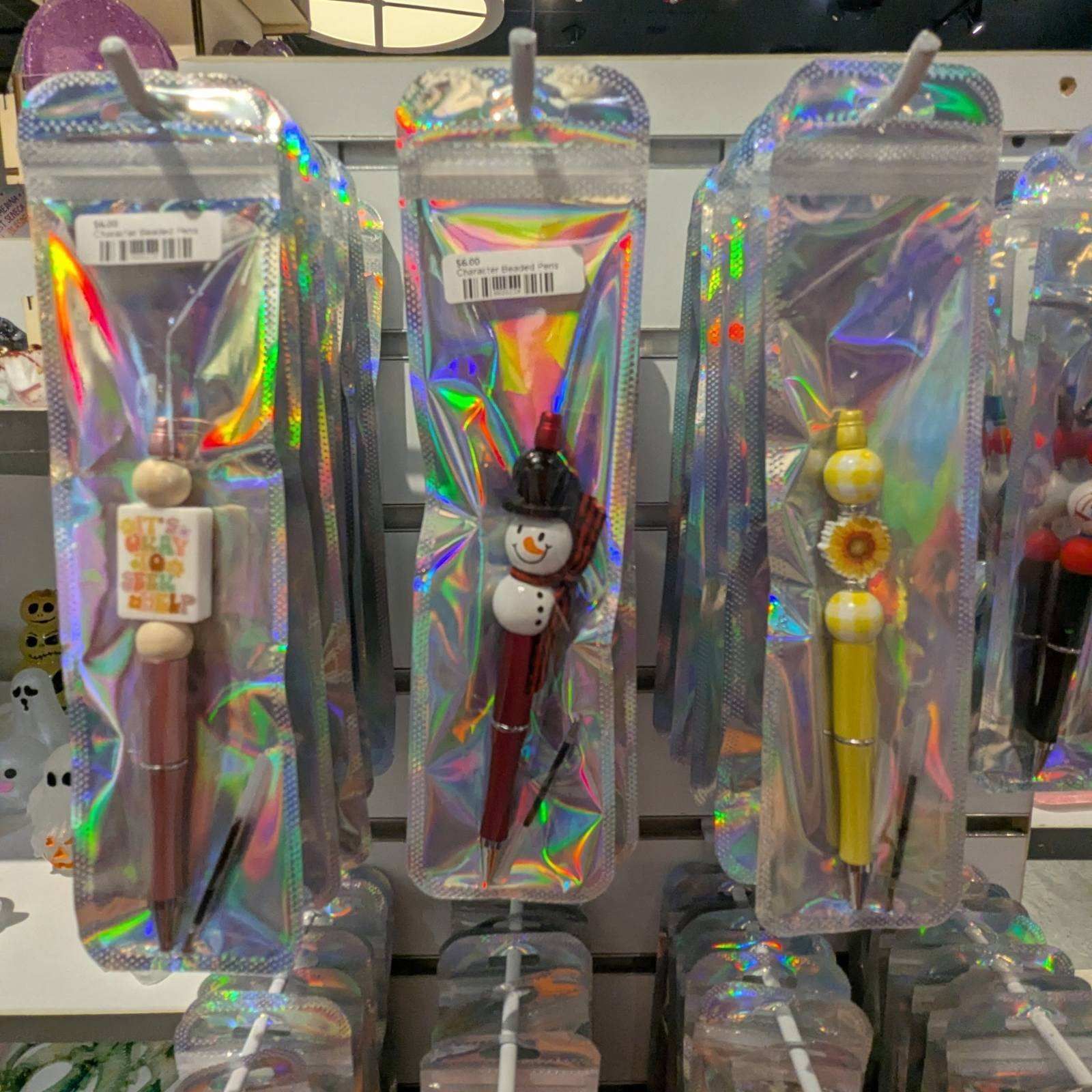 Pens in holographic packaging on display. Features include a snowman, sunflower, and other decorative elements.