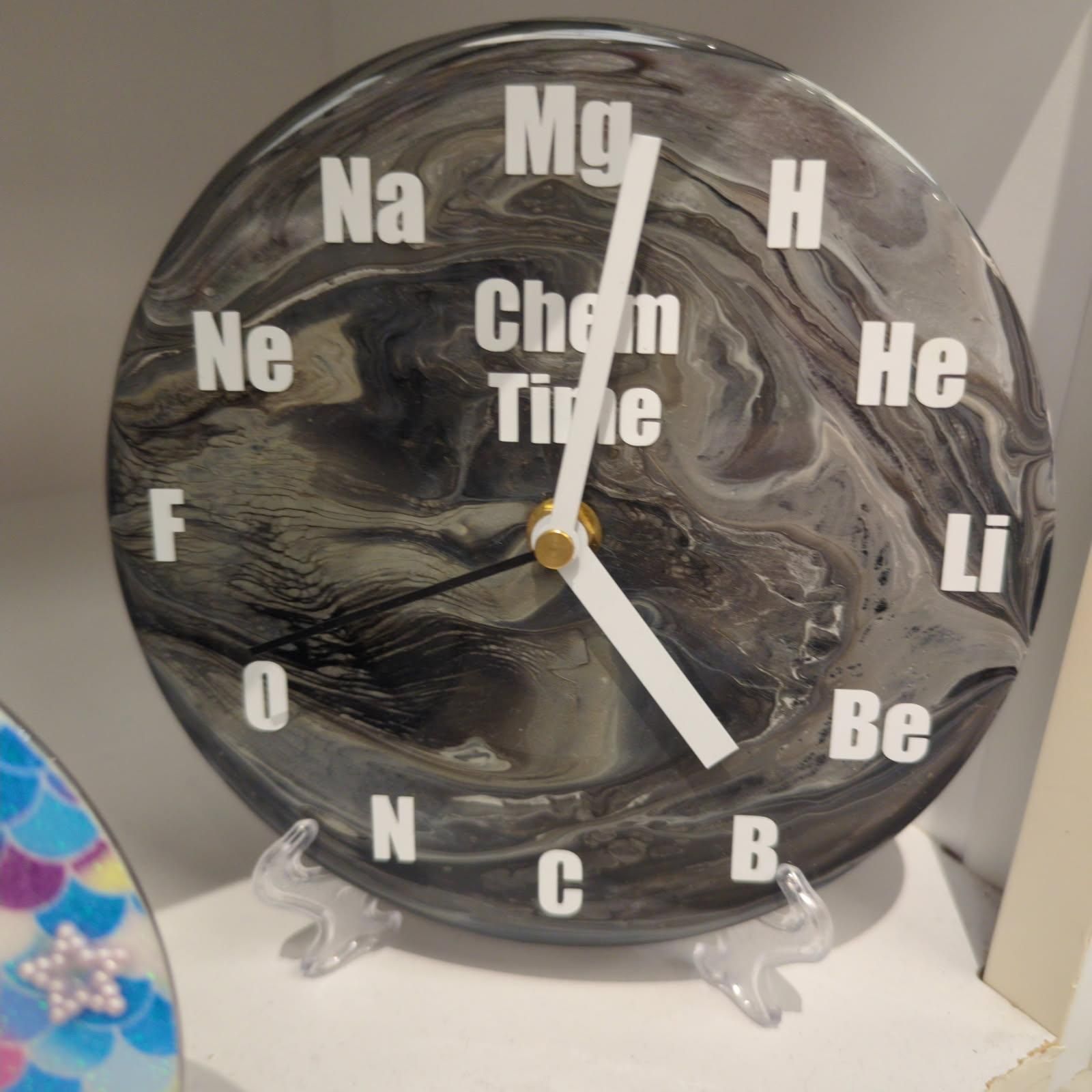Clock with a swirling black and white design. White periodic elements mark the hours; 