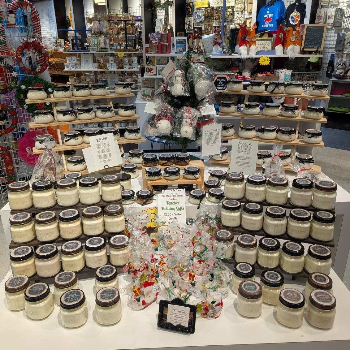 Display of candles in glass jars at a market stall, with wooden shelves and Christmas decorations.