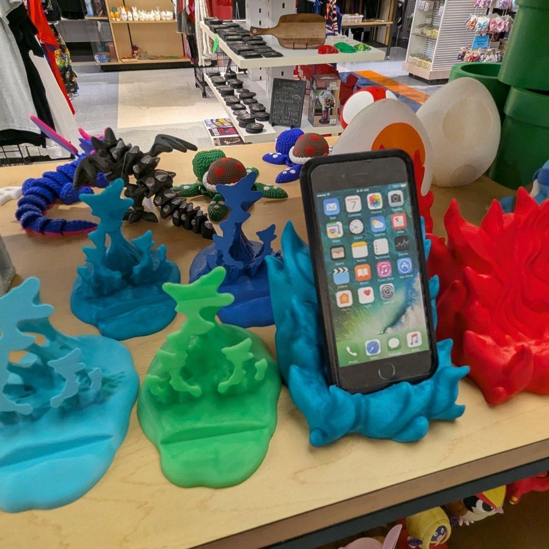 Display of colorful 3D-printed phone holders on a store shelf, one holding a phone.