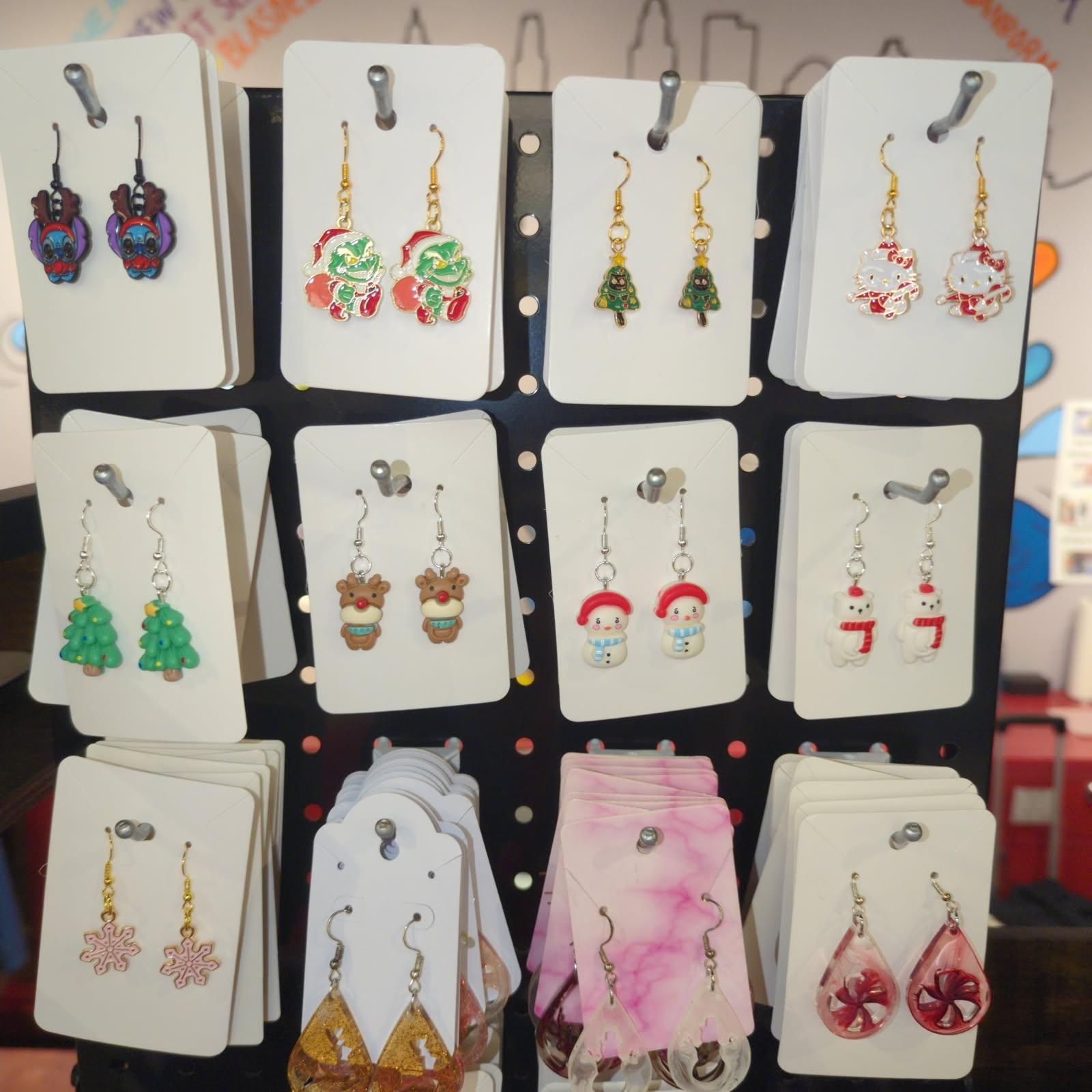 Earrings displayed on a black rack, featuring holiday-themed designs like owls, candy canes, and snowmen.
