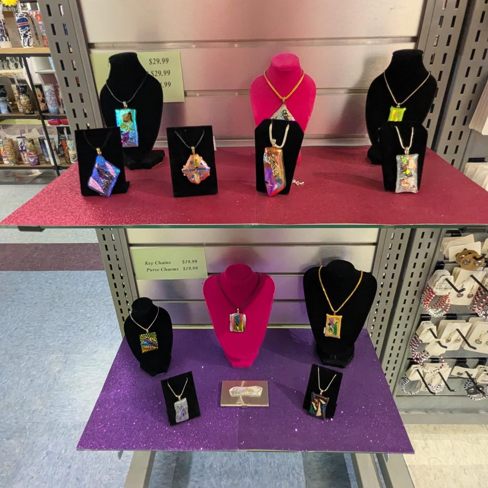 Jewelry display with colorful pendants on black and pink velvet necklace stands. Retail store setting.