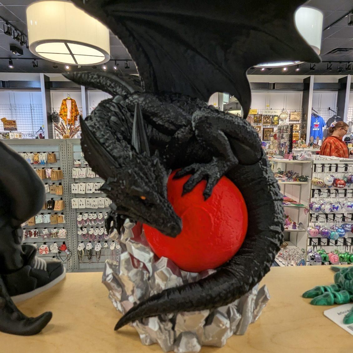 Black dragon statue clutches a red sphere, perched on a rocky base, in a shop setting.