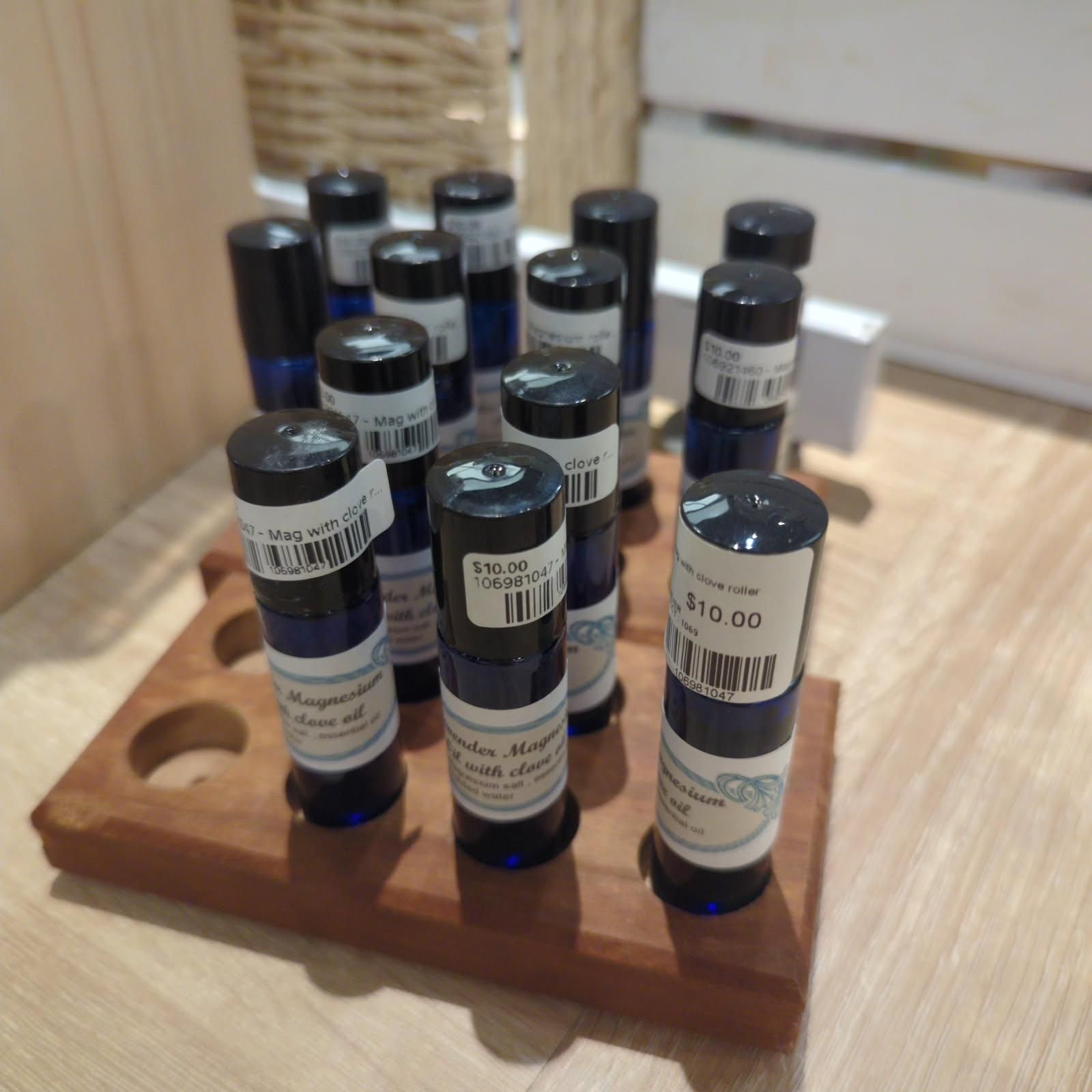 Blue-glass essential oil bottles in a wooden display stand. Each has a black cap and a price tag.