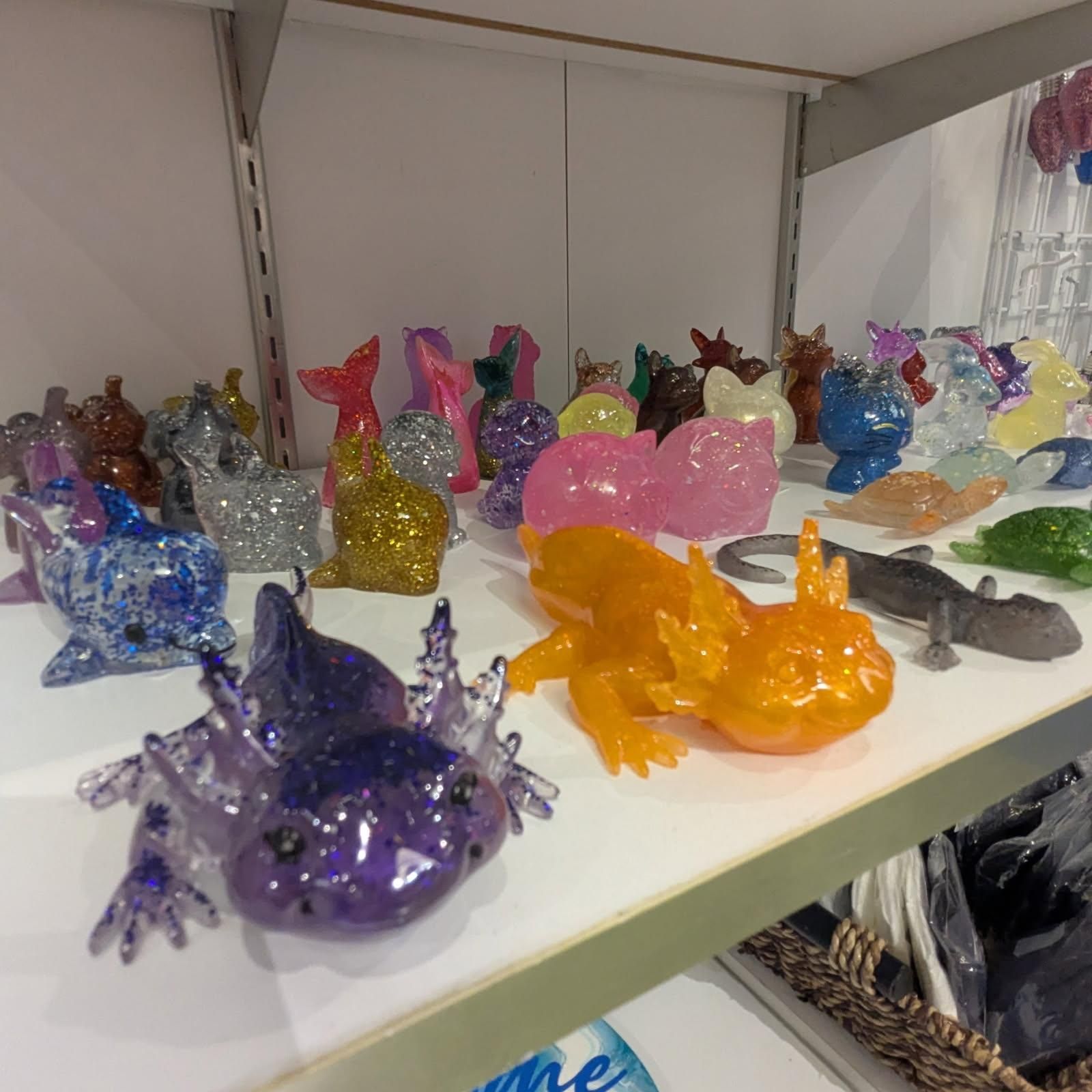 Shelf display of colorful resin axolotl figurines, featuring glitter, various colors.