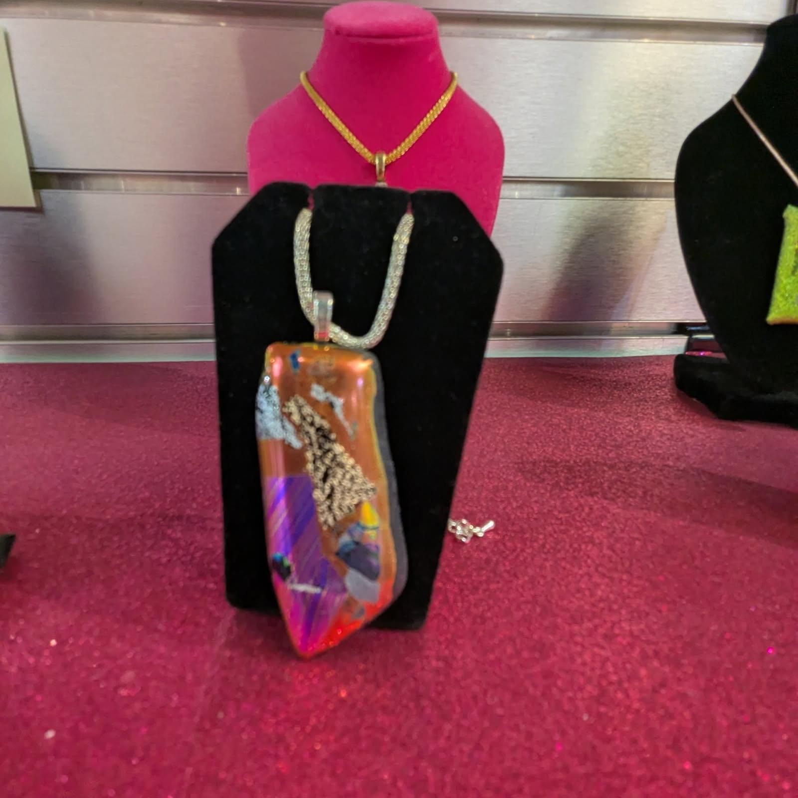Necklace with an abstract, colorful pendant displayed on a black stand.
