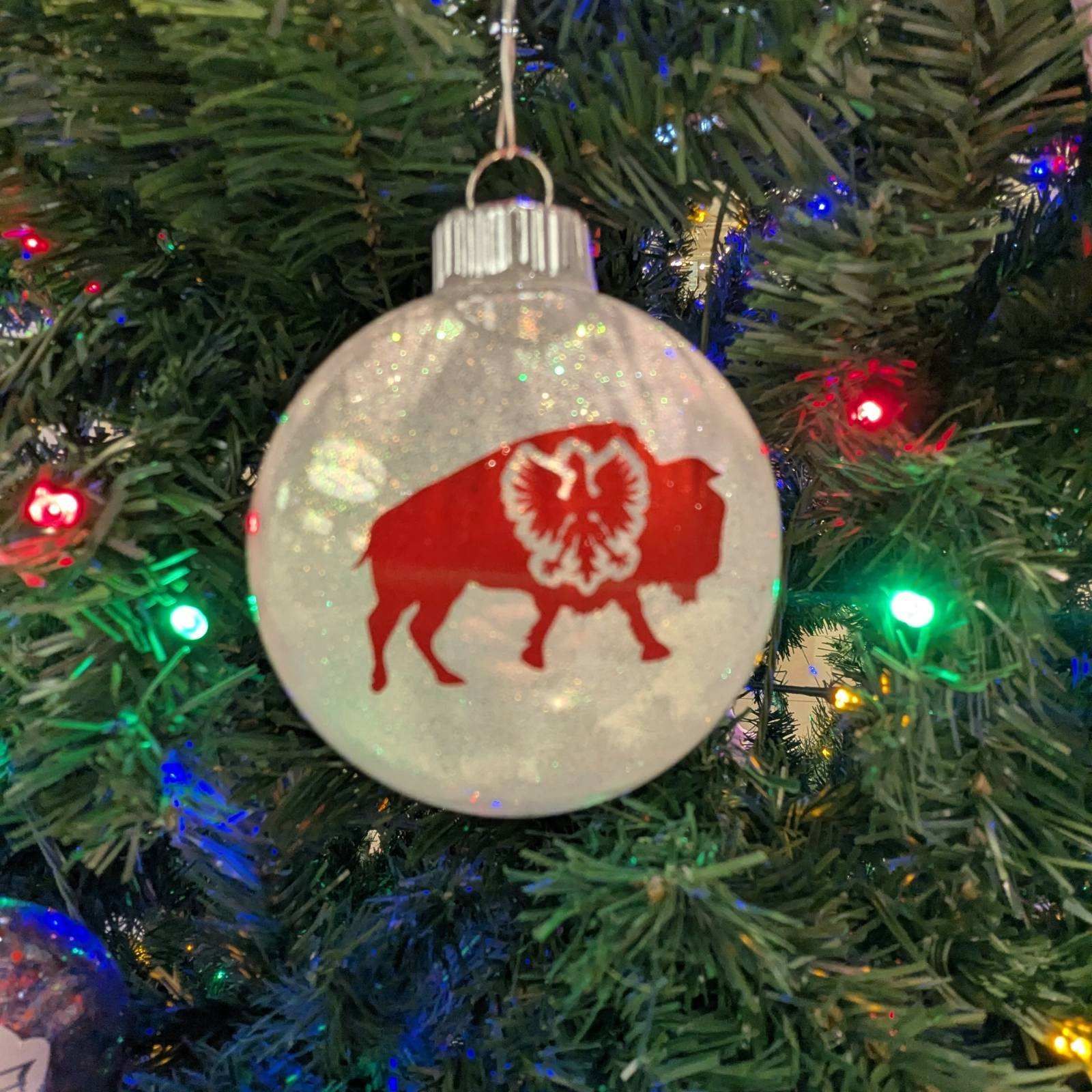 Christmas ornament with red bison silhouette and glitter, hanging in a decorated tree.