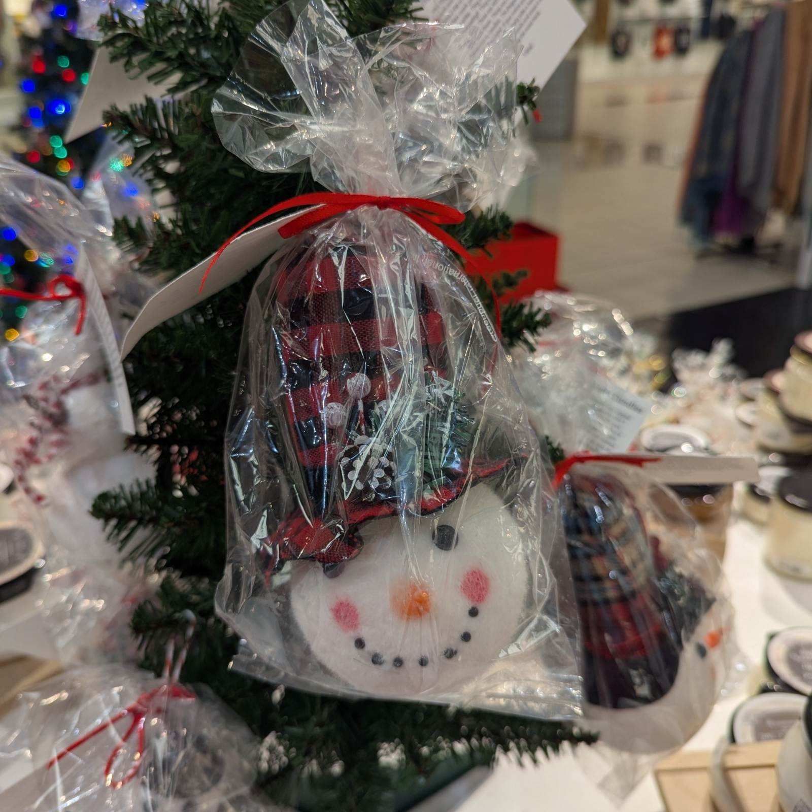 Snowman-shaped soap wrapped in plastic and tied with a red ribbon, displayed on a small Christmas tree.