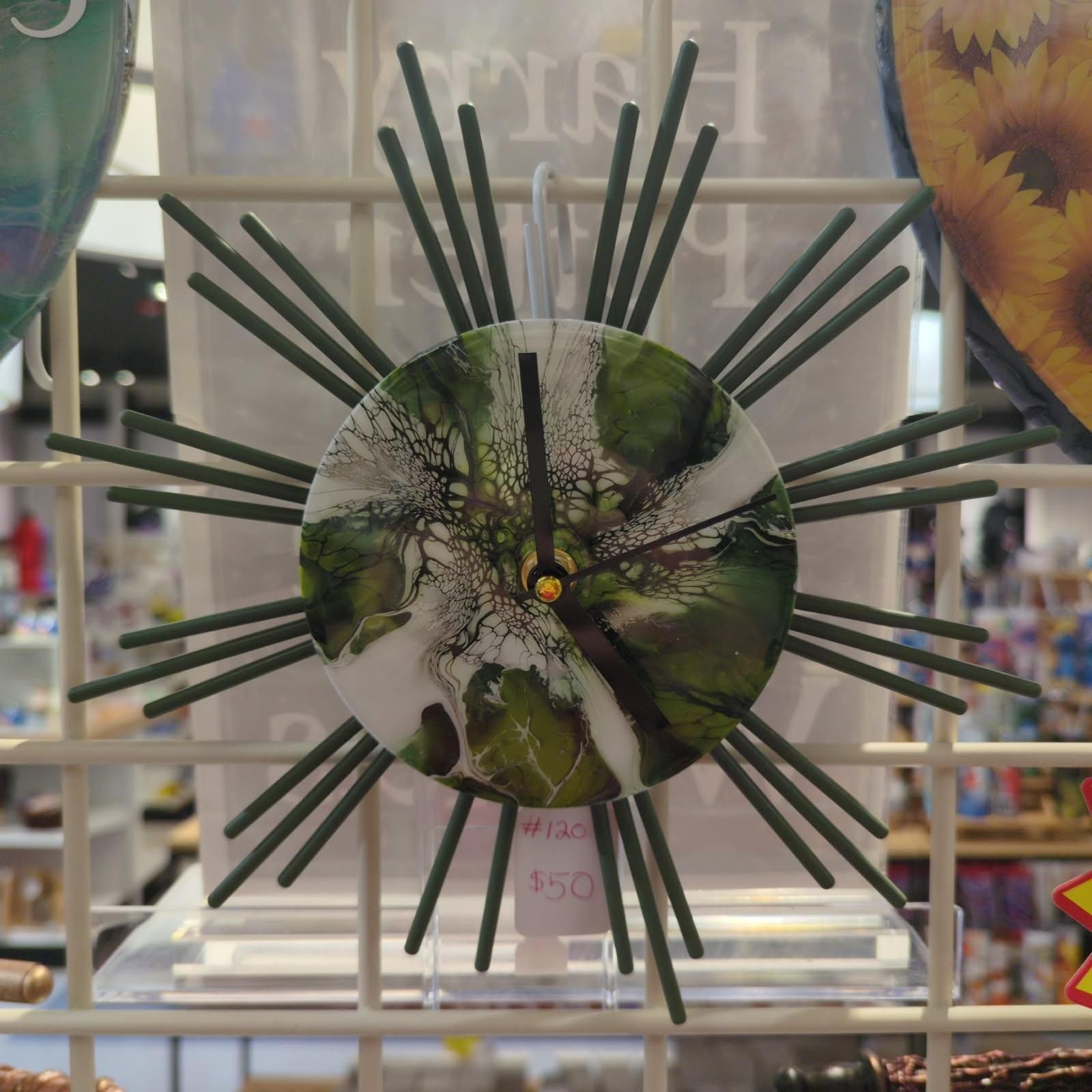 Green and white abstract-design wall clock with metal rod hands and dark green sunburst arms.