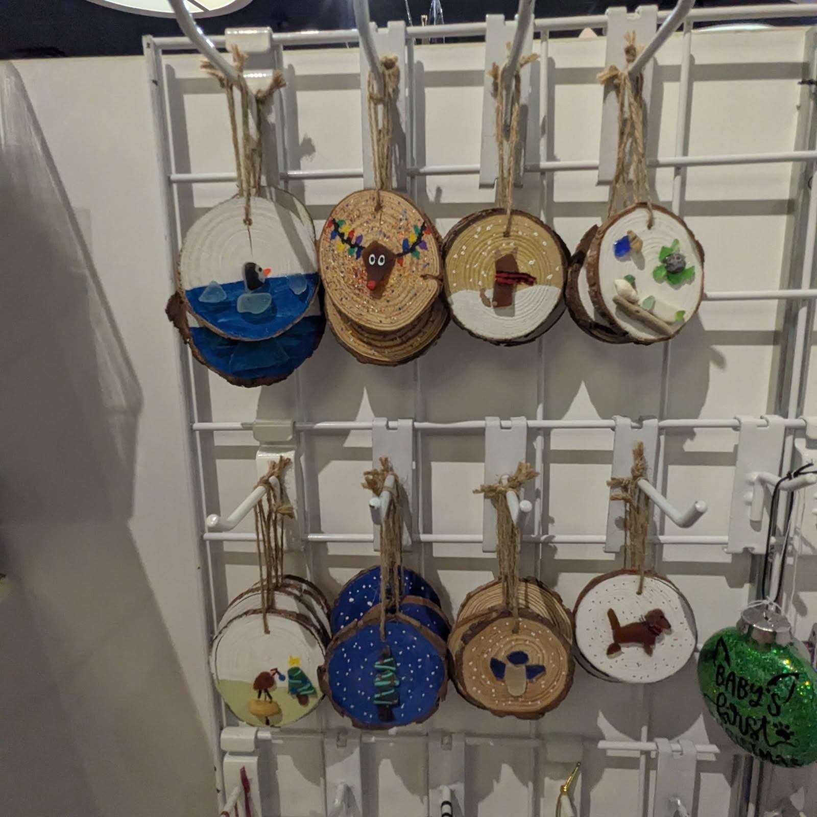 Ornament display: wood slice ornaments with various painted designs and twine hangers, displayed on a white grid.