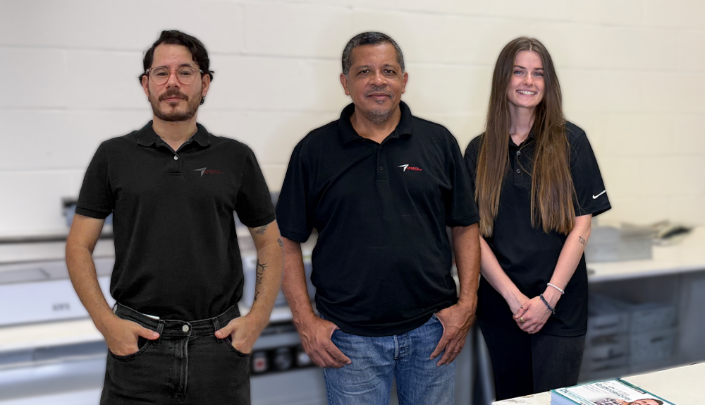 Three people in black polo shirts pose for a photo in a bright workspace with white walls and equipment surfaces.