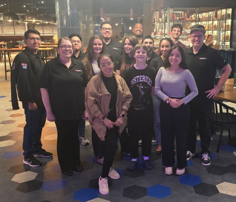Group of people posing together in a modern venue with blue and gray accents, smiling.