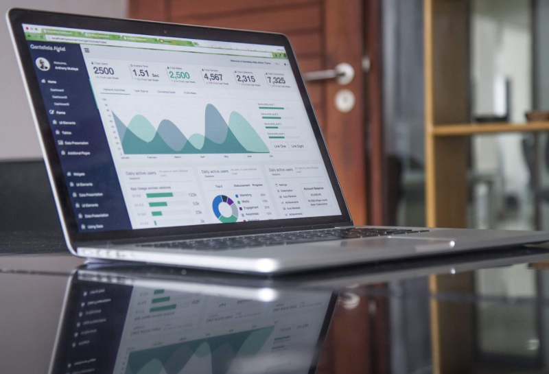 A laptop sits on a reflective table, displaying a business analytics dashboard with various charts and data visualizations.
