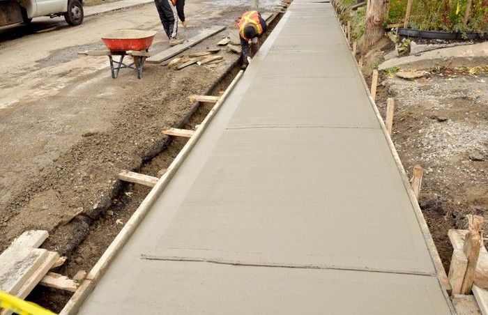 Construction workers pouring concrete for a sidewalk, viewed from a high angle.
