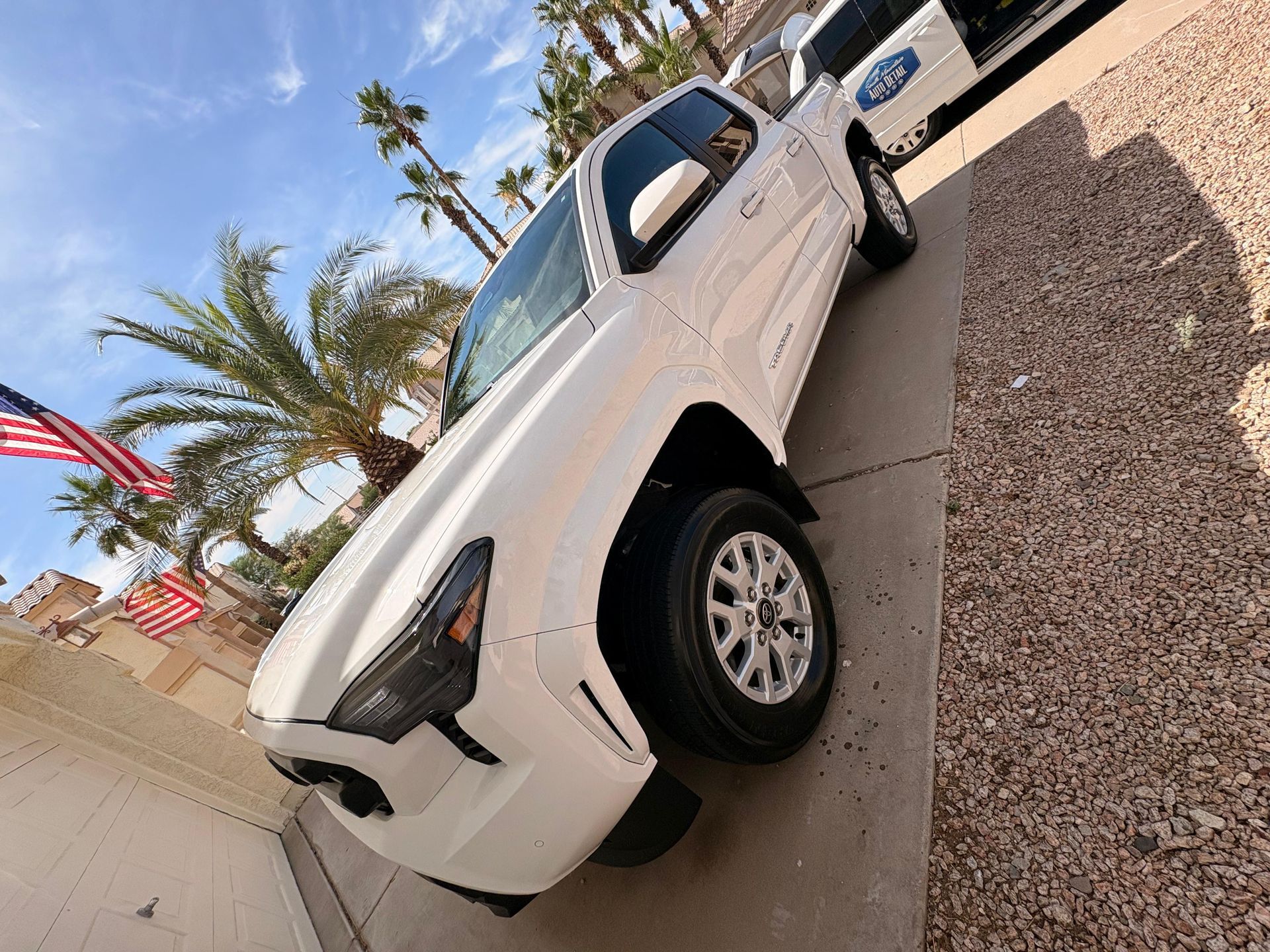 White pickup truck parked on a gravel lot near palm trees and flags