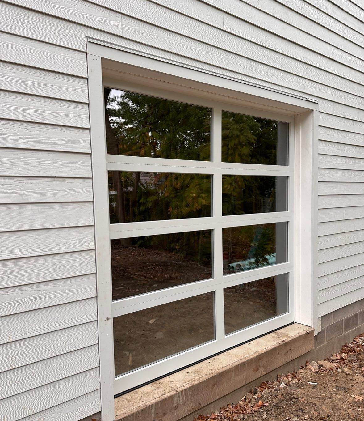 White paneled garage door on a white siding building, showing the reflection of trees.