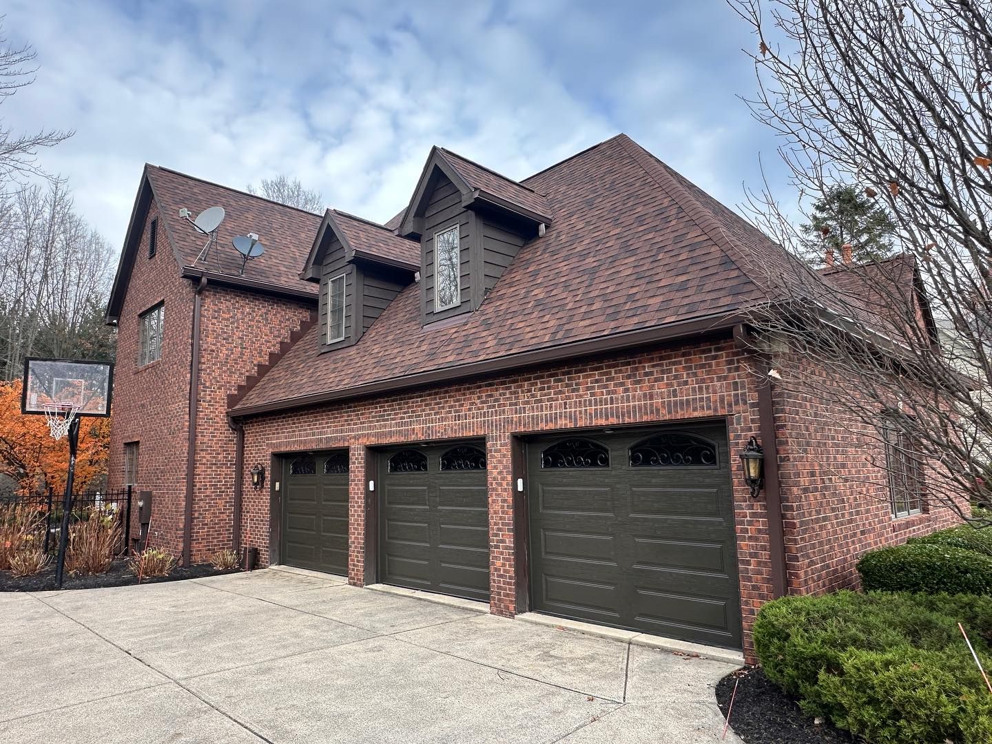 Brick house with brown garage doors, roof, and dormers; basketball hoop.