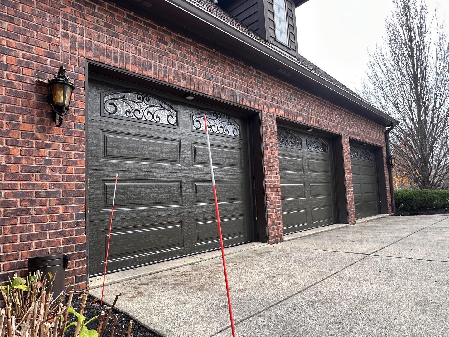 Three dark green garage doors on a brick building, with a light pole.