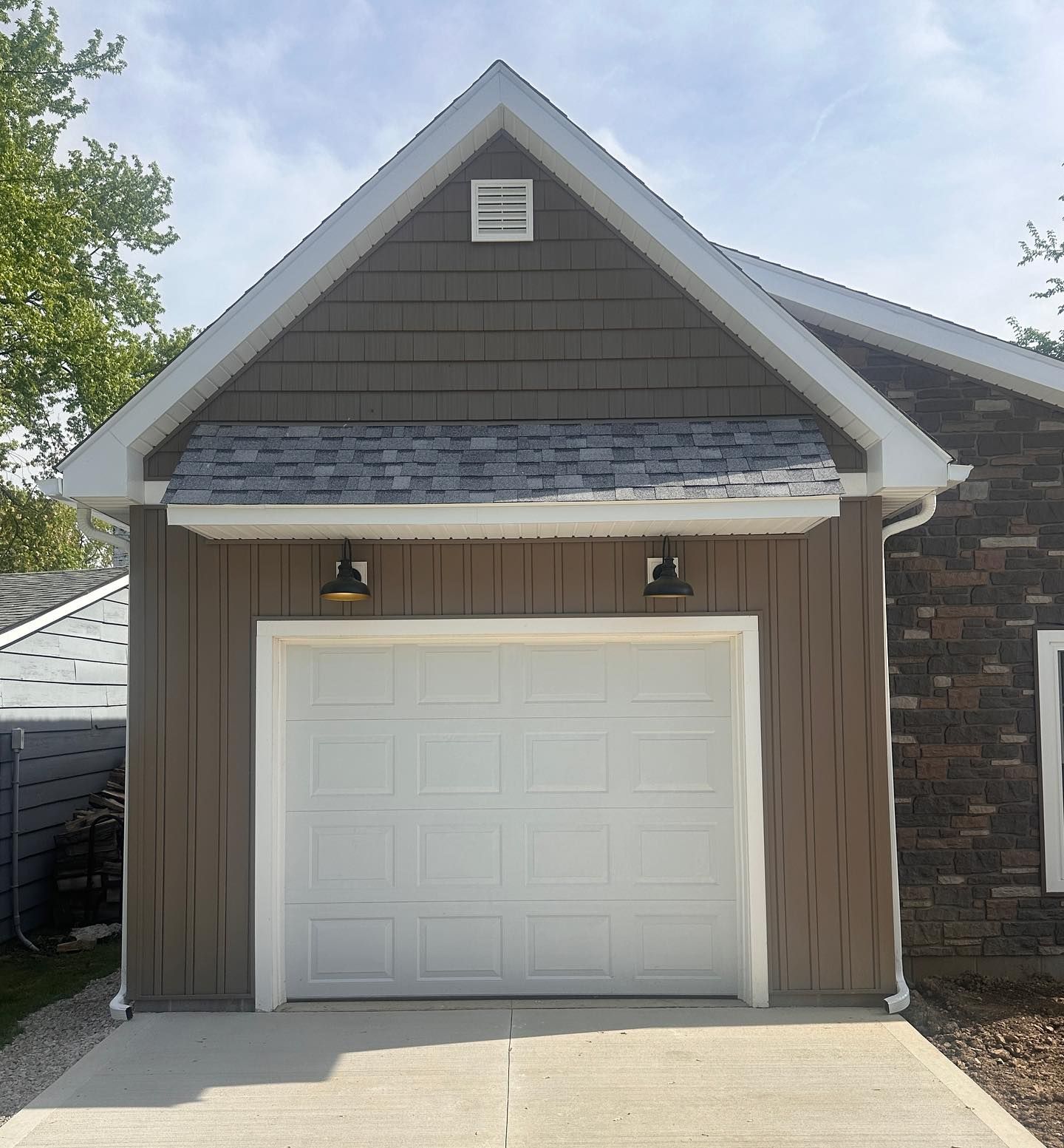 A garage with a white door, brown siding, and gray roof. Two black lights above the door.