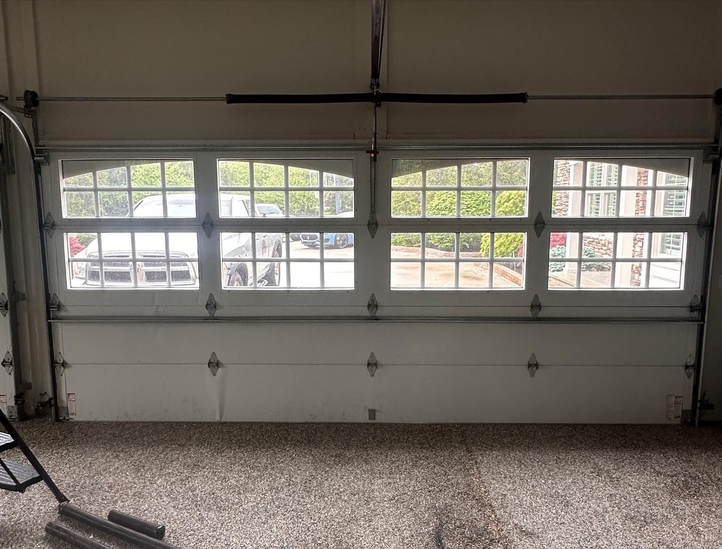 White garage door with arched windows, partially open, revealing cars outside.
