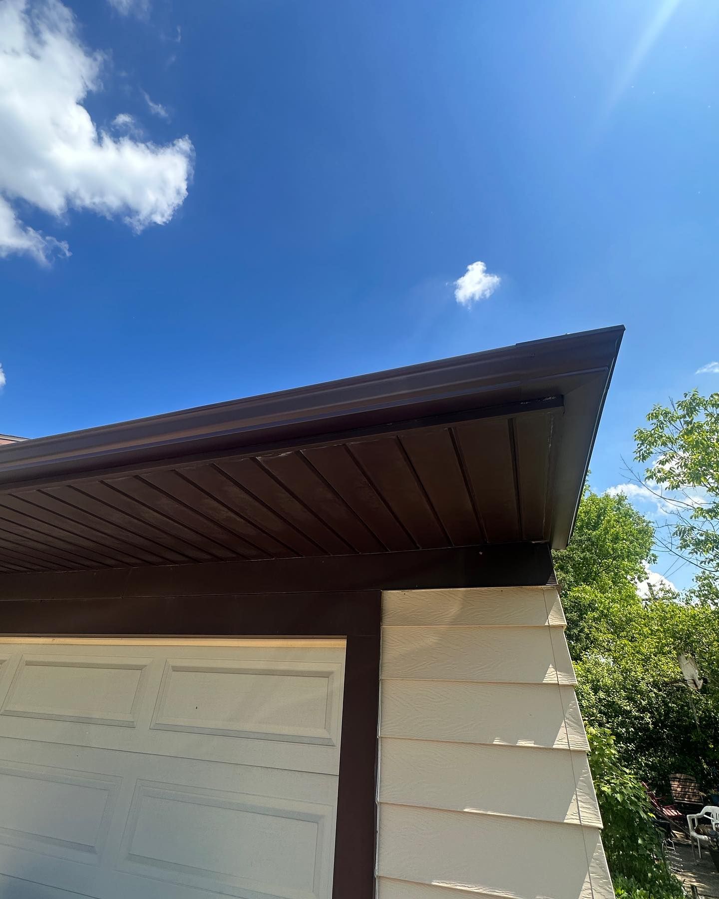 Brown eaves and fascia on a white garage, against a blue sky with clouds.