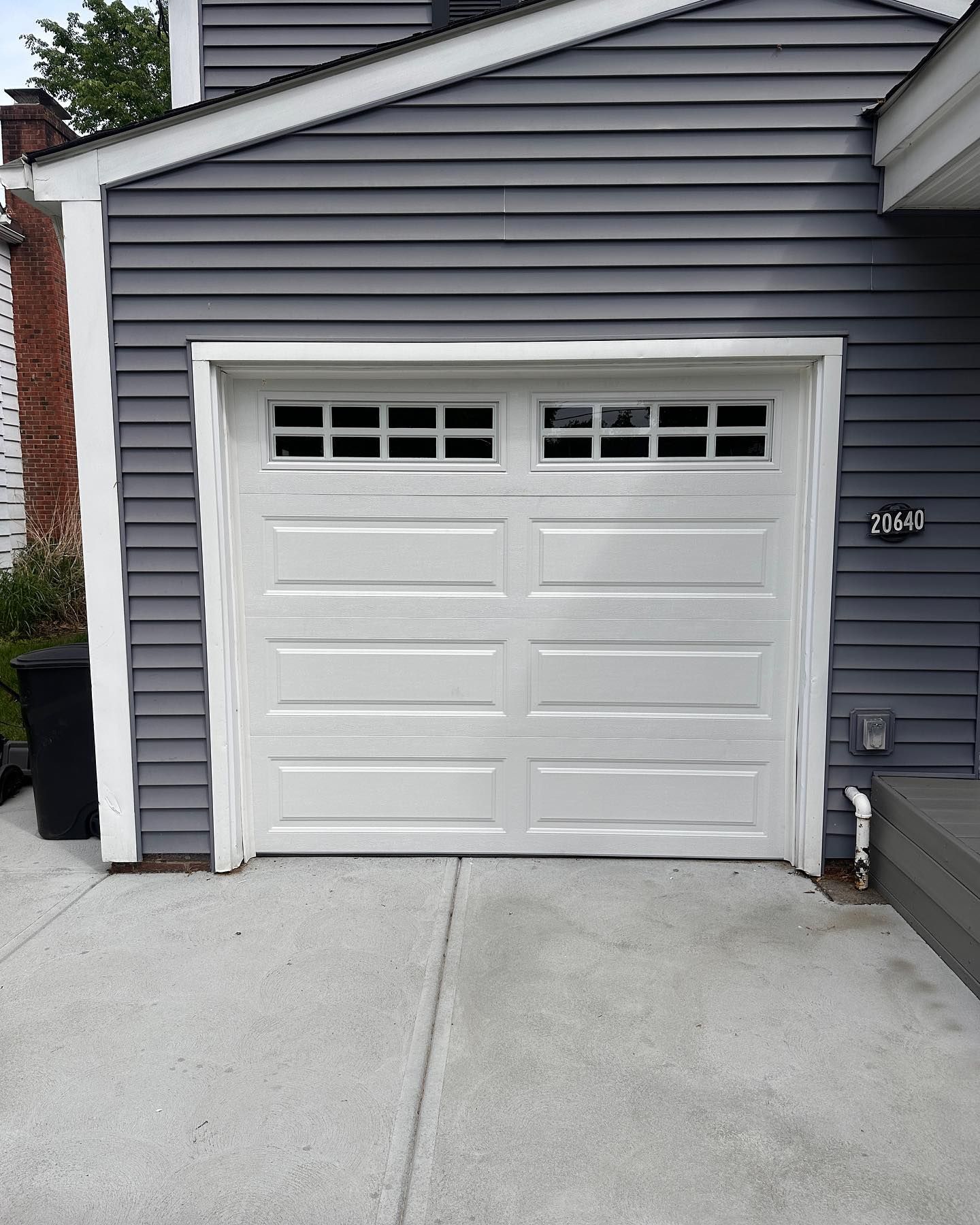 White garage door with rectangular windows, gray siding, and concrete driveway.