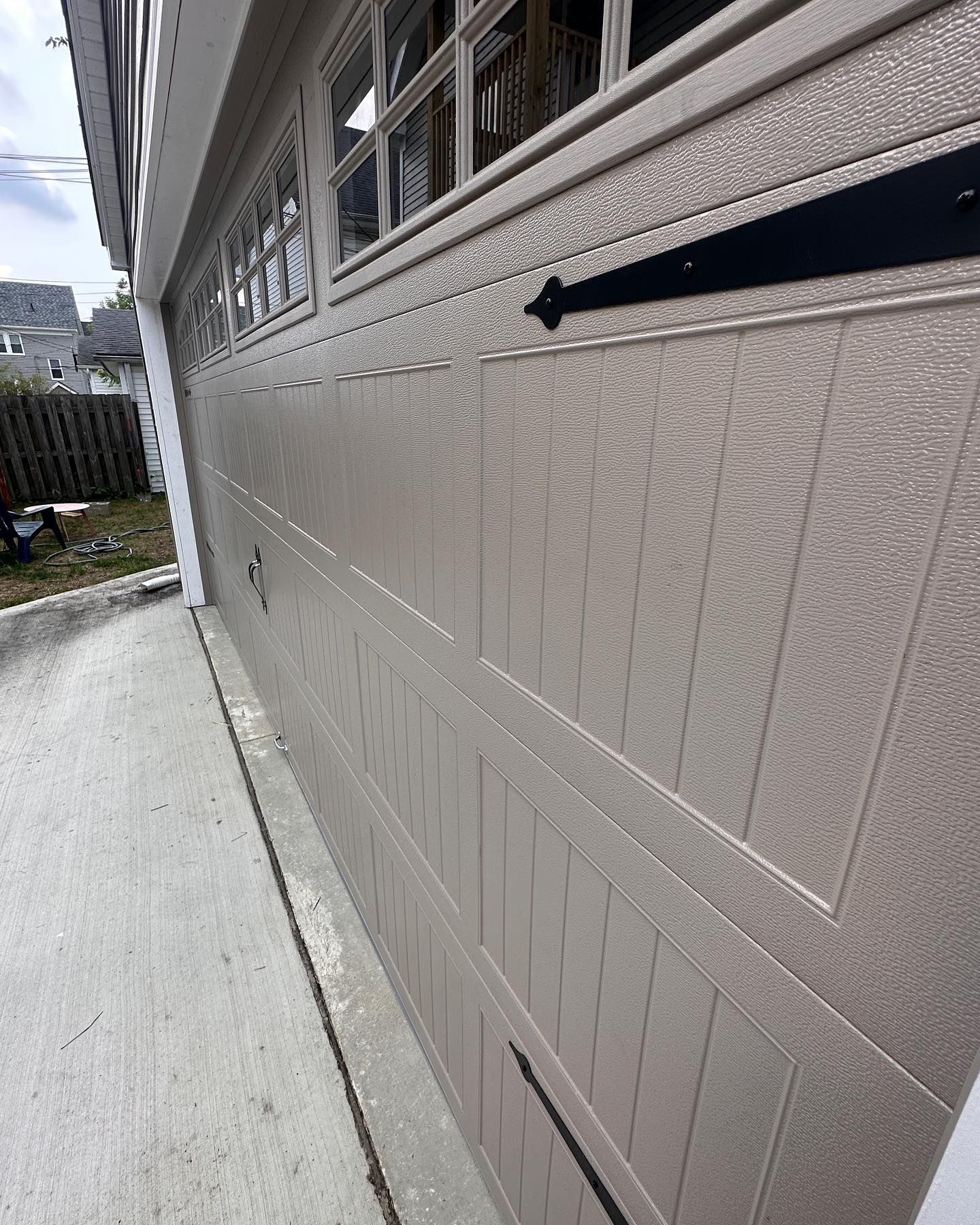 Tan garage door with decorative hardware, a window above, and a concrete driveway.