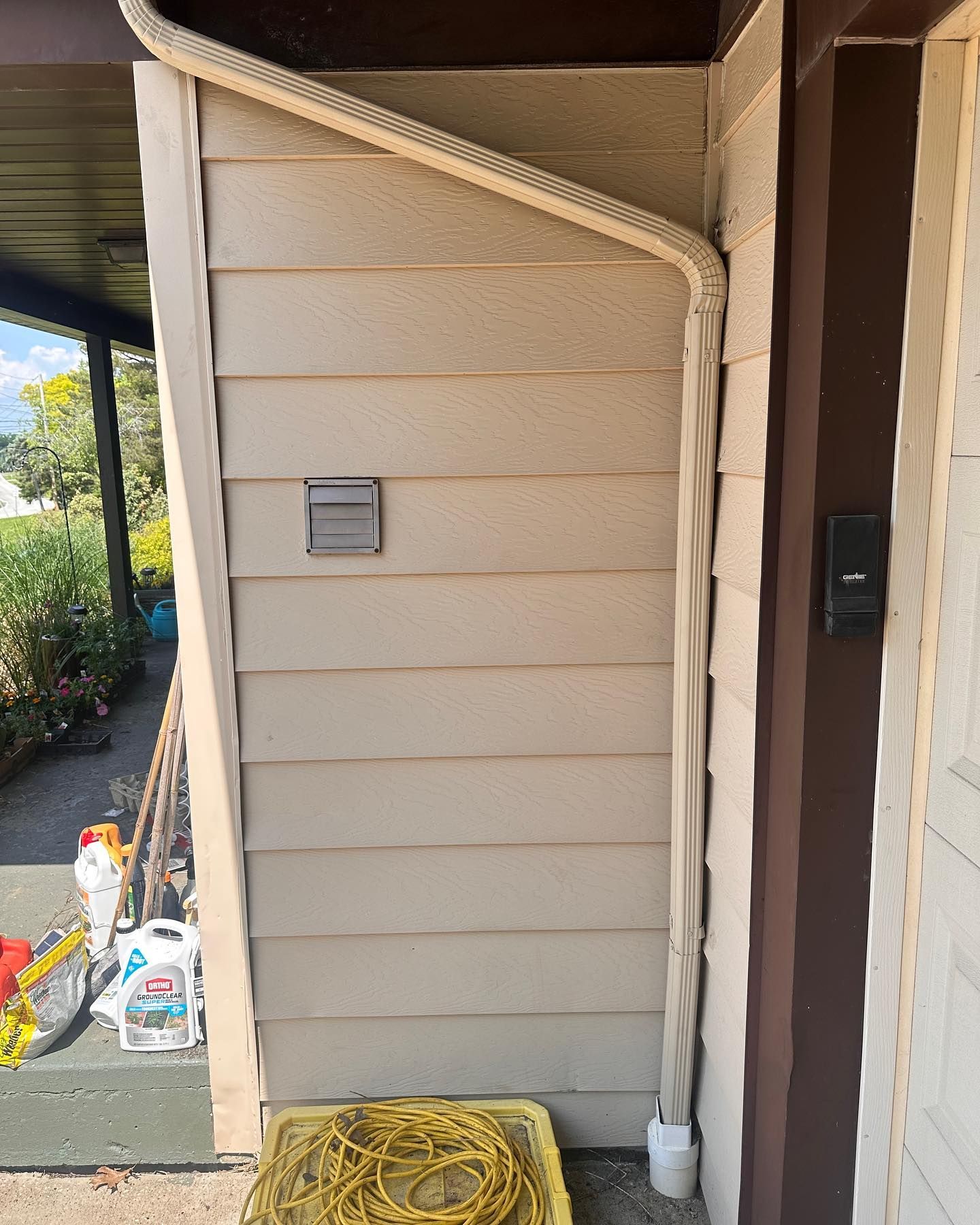 Beige siding on a building exterior with a vent, electrical conduit, and a coiled yellow cord on the ground.