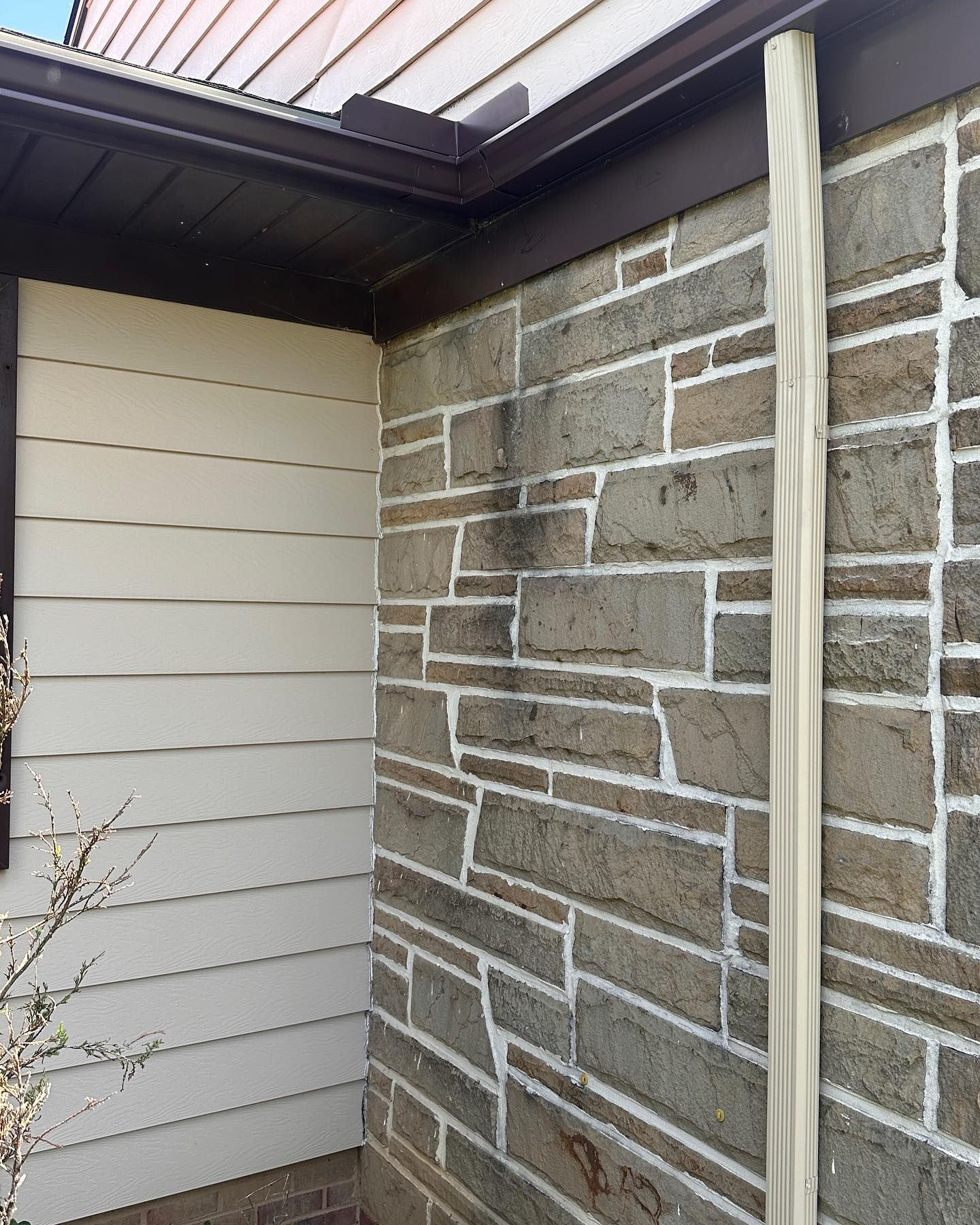 Stone wall with dark stain below gutter, light siding to the left, downspout.
