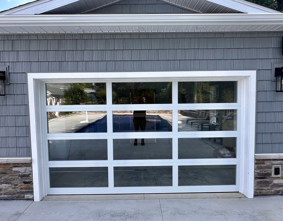 White-framed glass garage door reflecting a person standing in front of it; gray house exterior.
