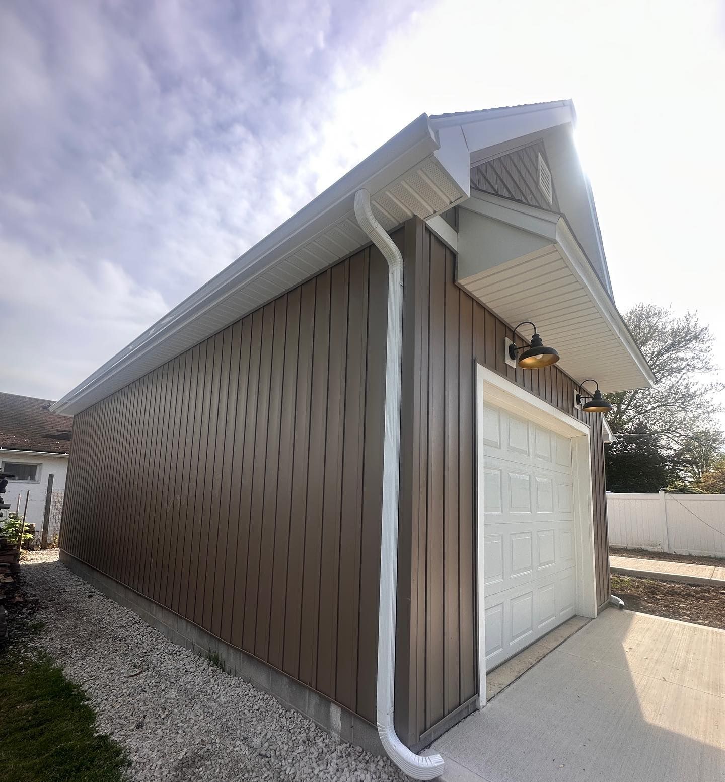 Brown-sided garage with white trim, gutter, and garage door on a concrete pad.