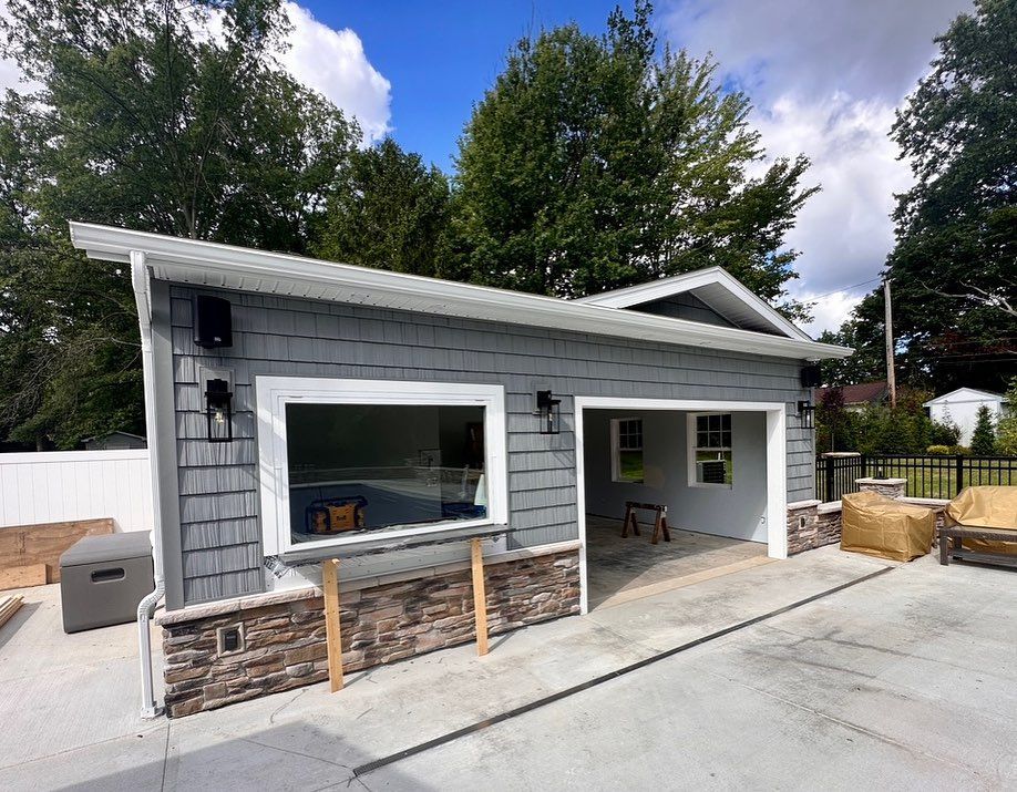 Gray and stone garage exterior with large window, two garage doors, and a concrete driveway under a blue sky.