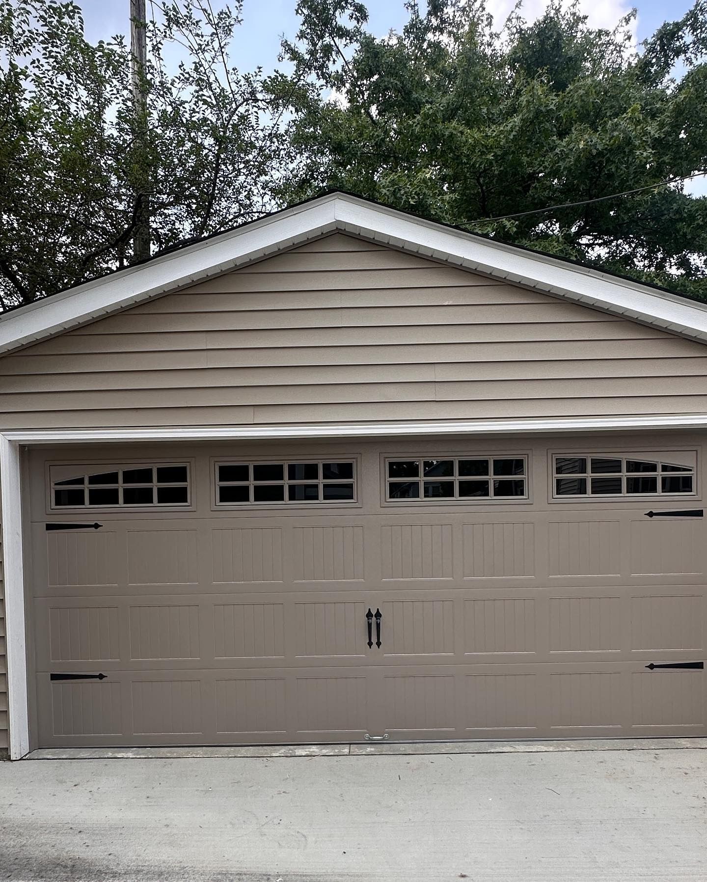 Tan garage with a beige garage door, black hardware, and a gable roof.