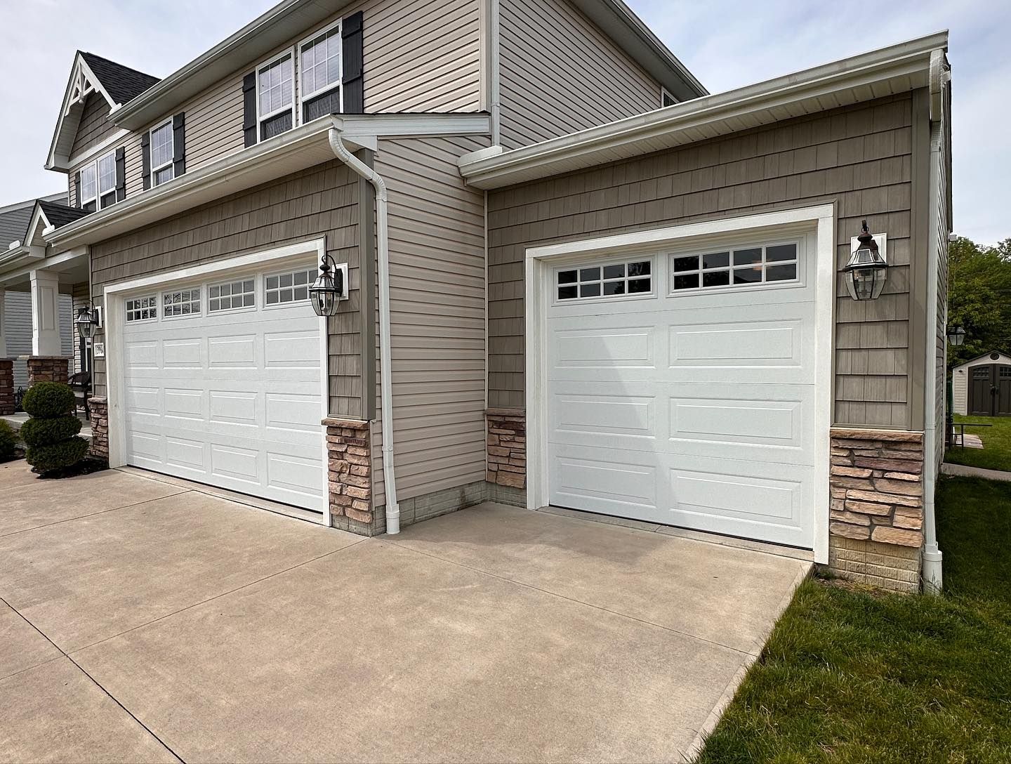 Two white garage doors with stone accents on a tan house with a concrete driveway and grass.