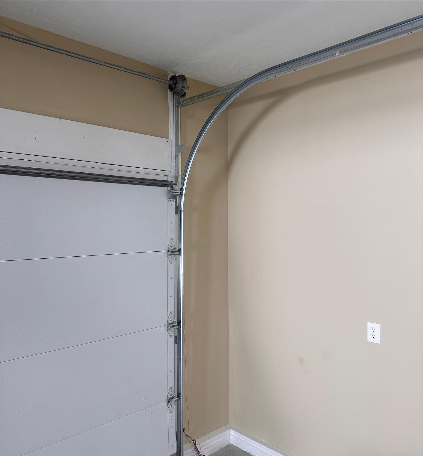 Garage door panel with curved track along a tan wall. The door is partially open.