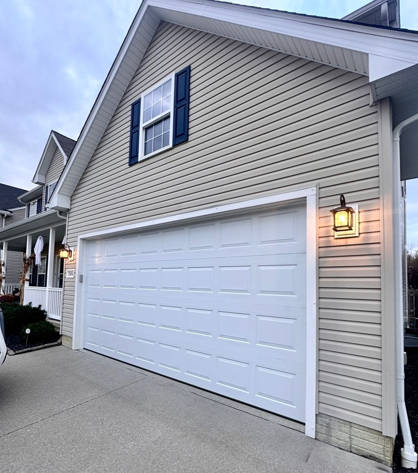 Garage with white door, tan siding, blue shutter, and outdoor light.