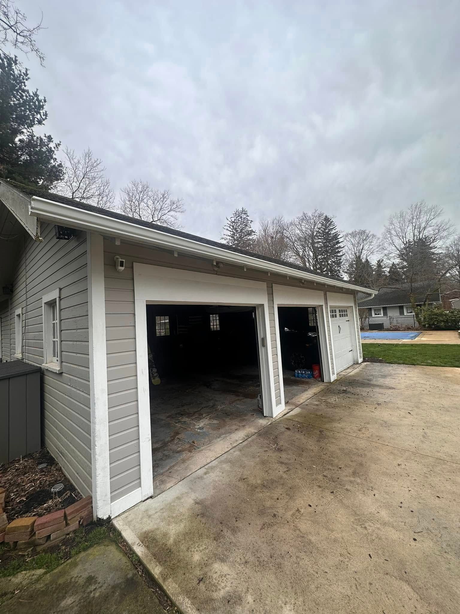 Gray garage with open doors, concrete driveway, cloudy sky.