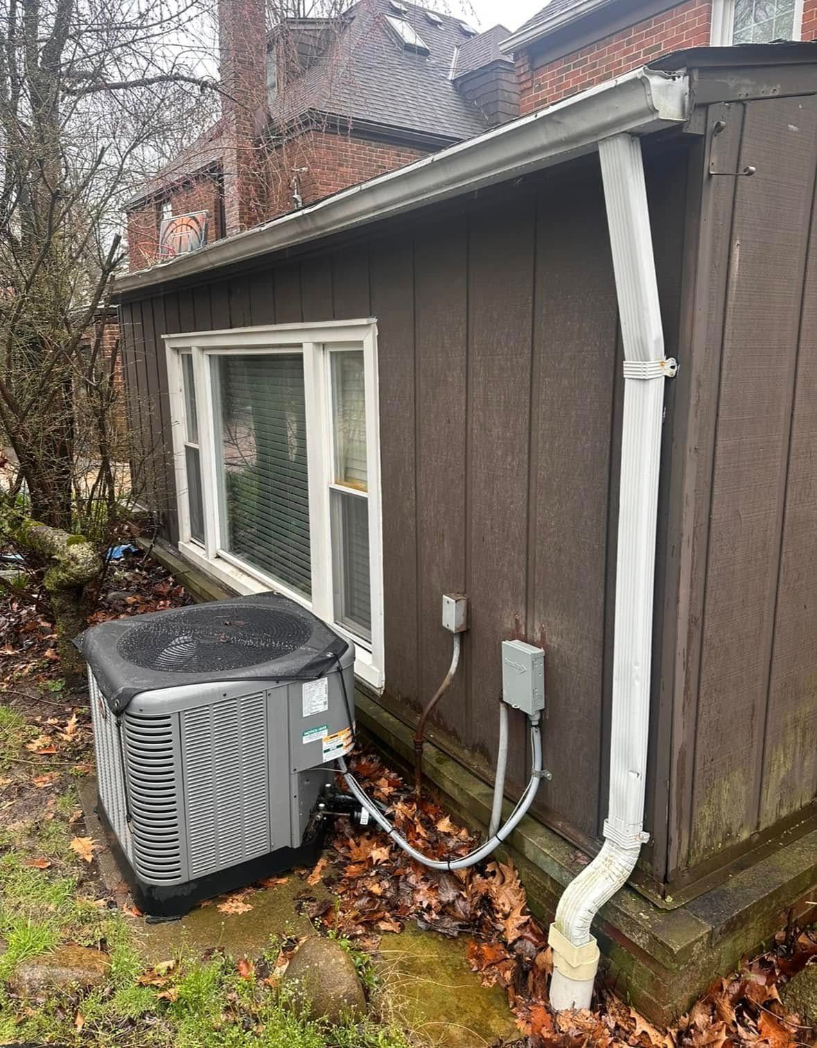 HVAC unit outside a brown building with a window and a white downspout.
