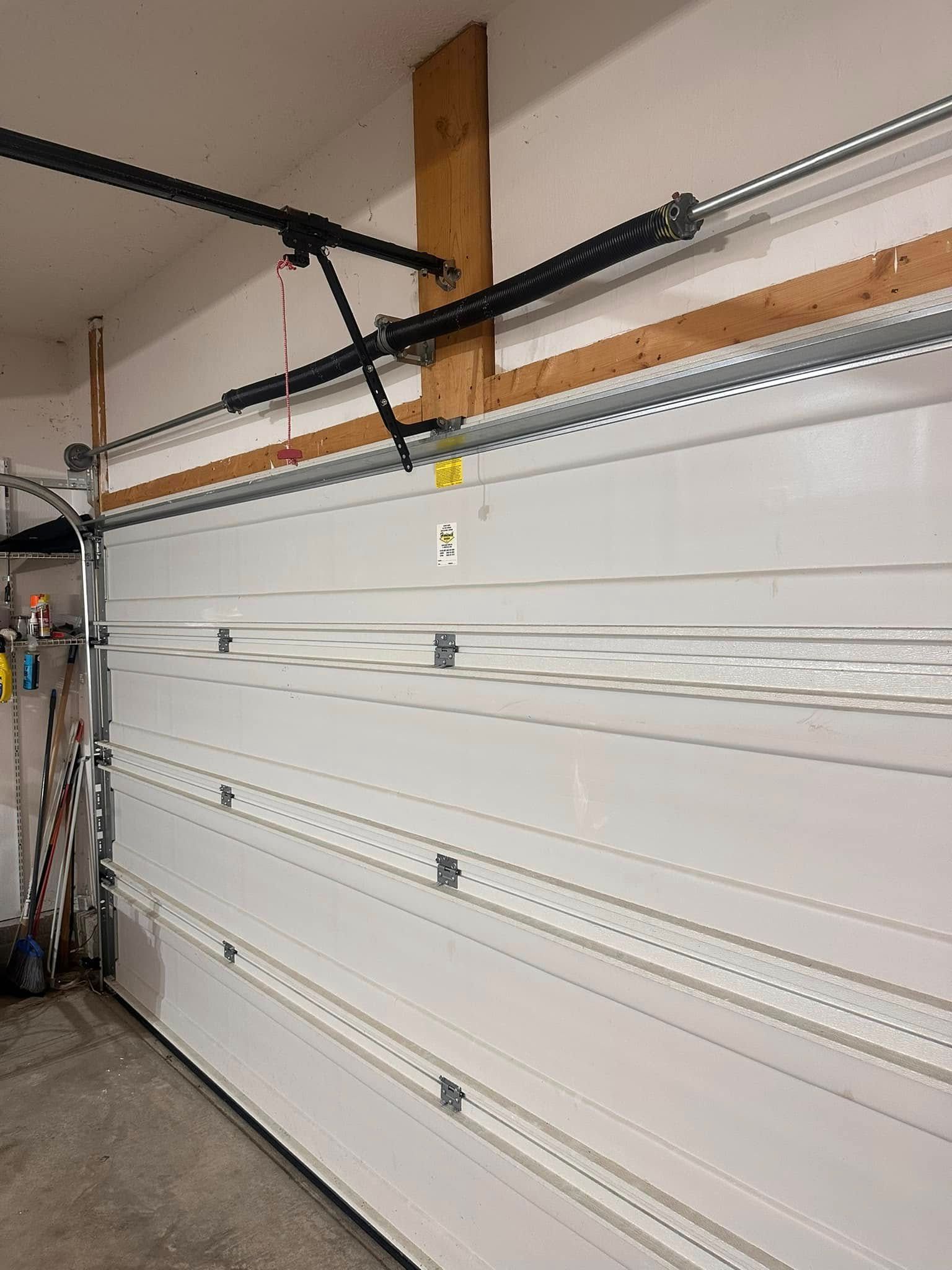 White garage door with a black opener on a wall with a wooden structure.