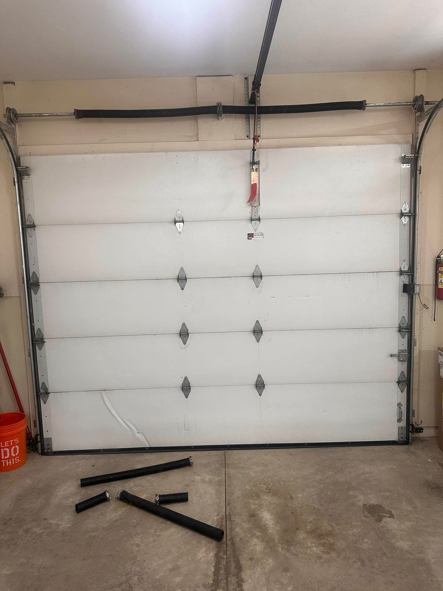 A white garage door with a broken section and parts on the floor of a garage.