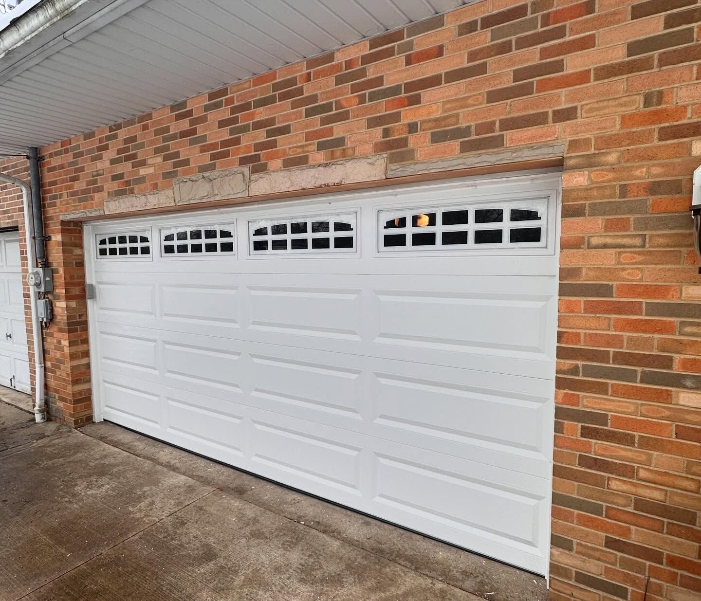 White garage door with windows, set in a brick building.