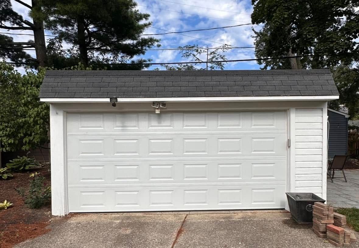 White garage with a closed door under a dark shingled roof, on a concrete driveway.