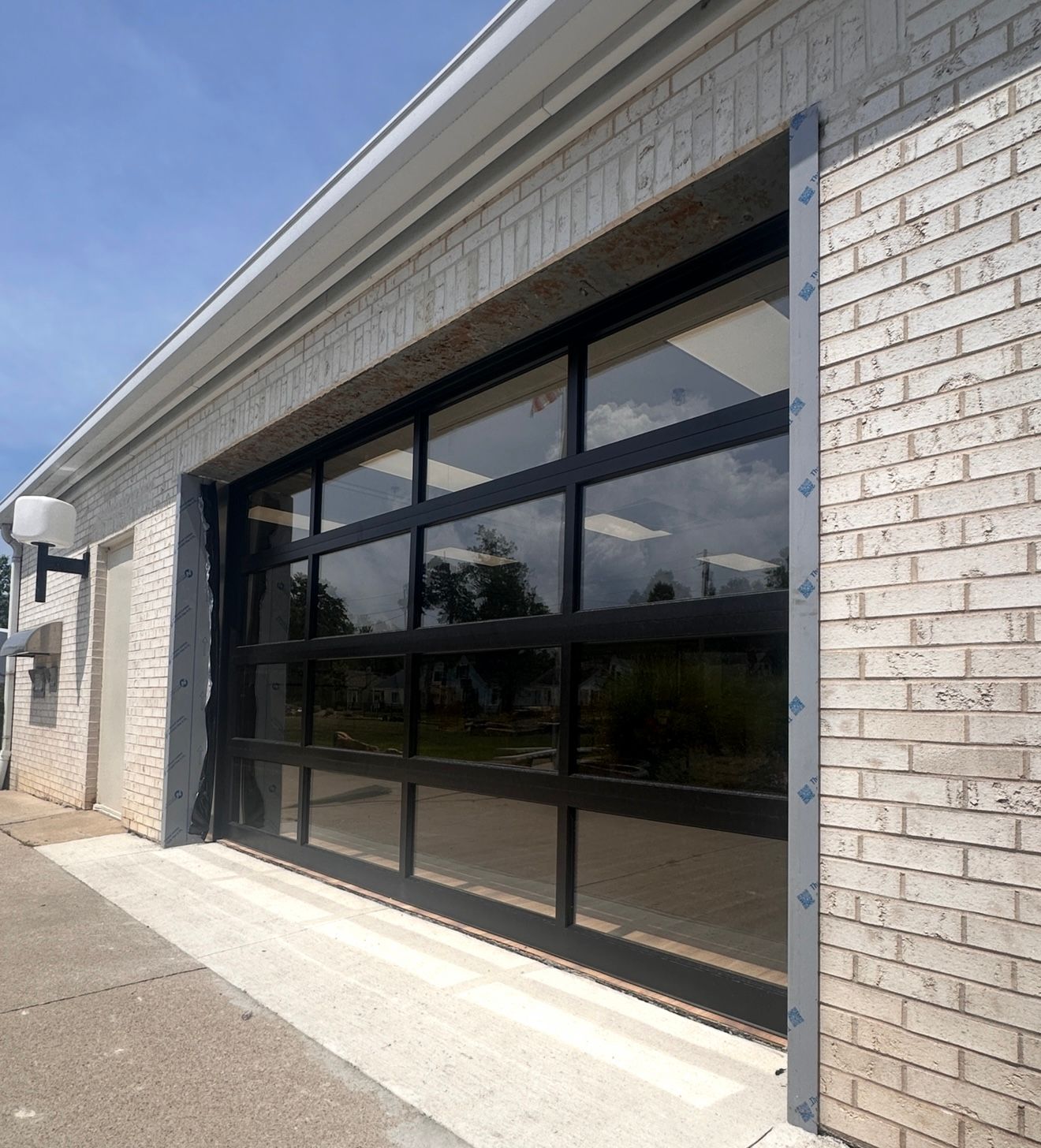 Modern glass garage door with black framing and brick exterior.
