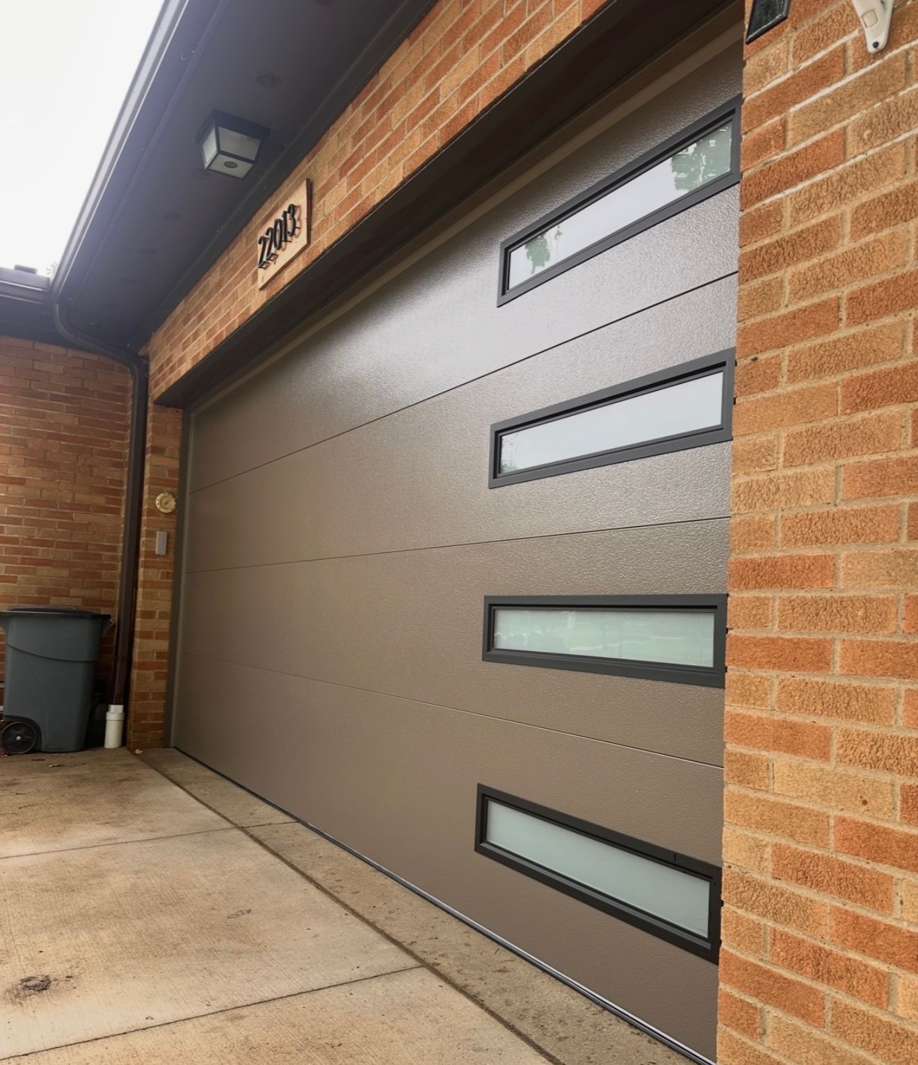 Brown garage door with horizontal lines, rectangular windows, and brick exterior.